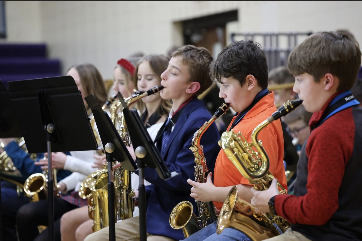 A row of young musicians in semi-formal clothing focus intently on playing their golden saxophones during a performance.