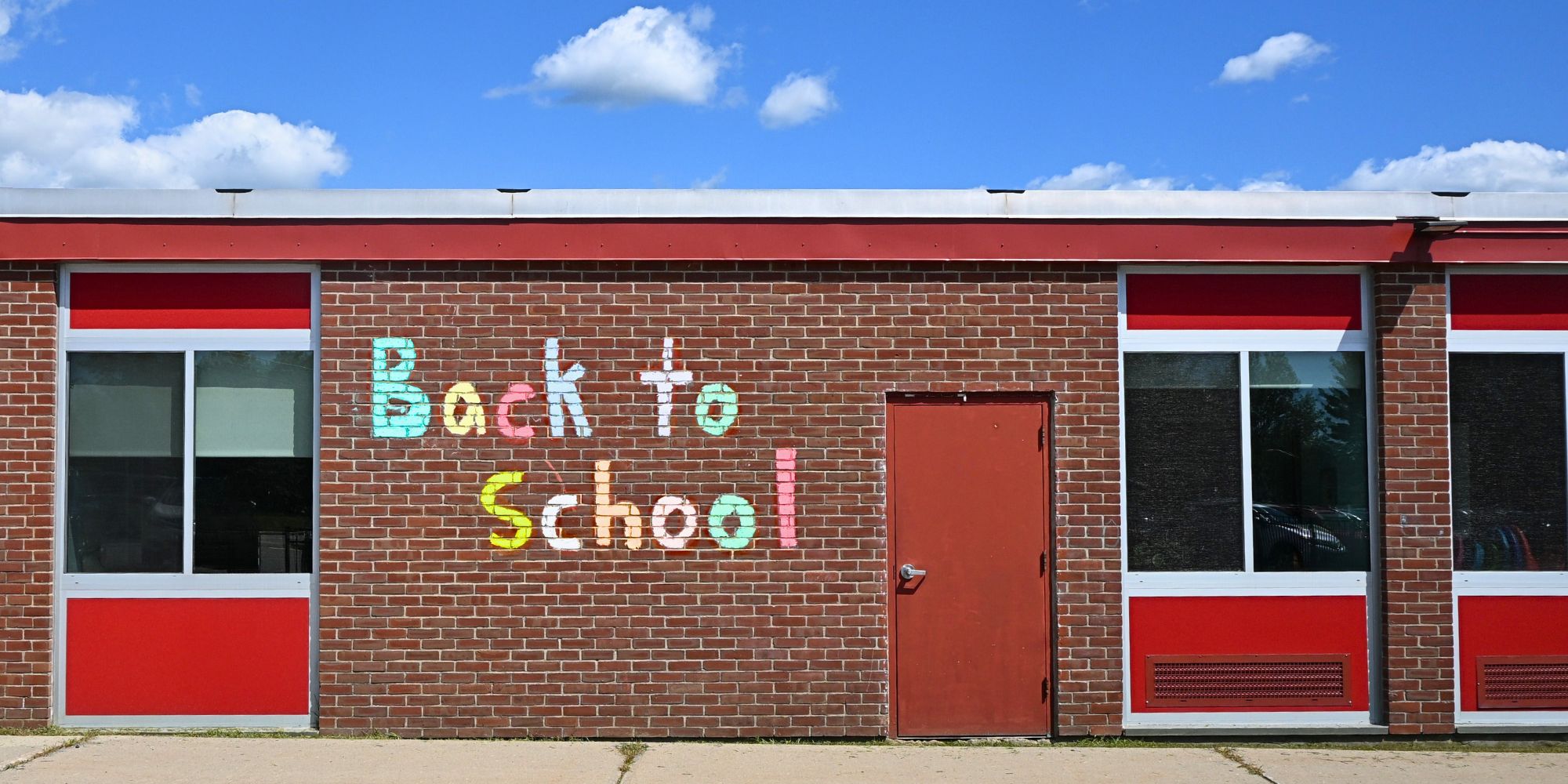 A brick building with "Back to School" written on it. The building has red trim, glass windows, and a red door.