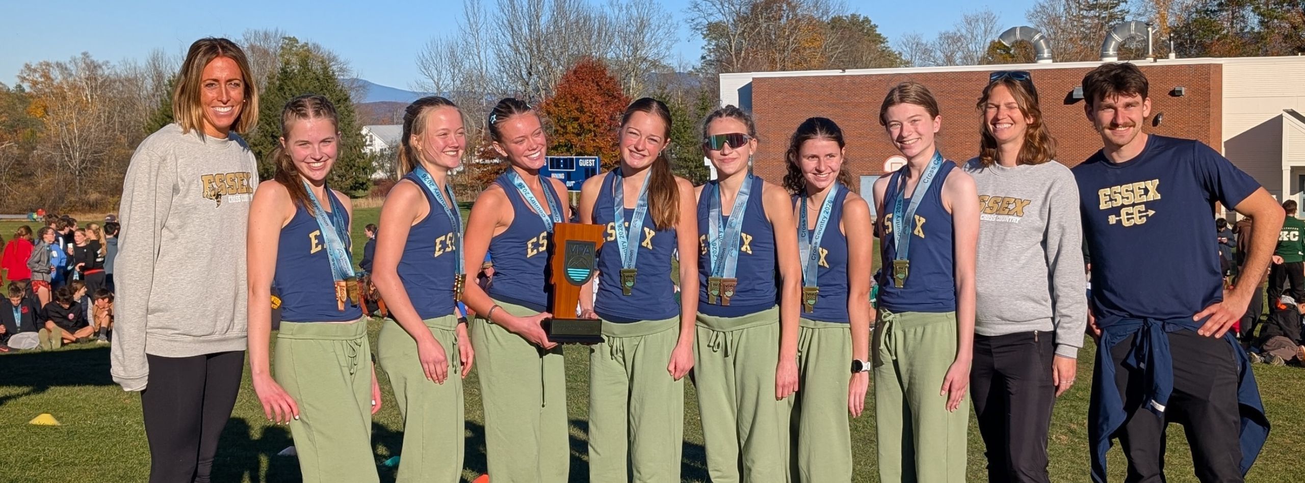 Group of athletes wearing blue shirts and green pants, with medals, standing on a field.