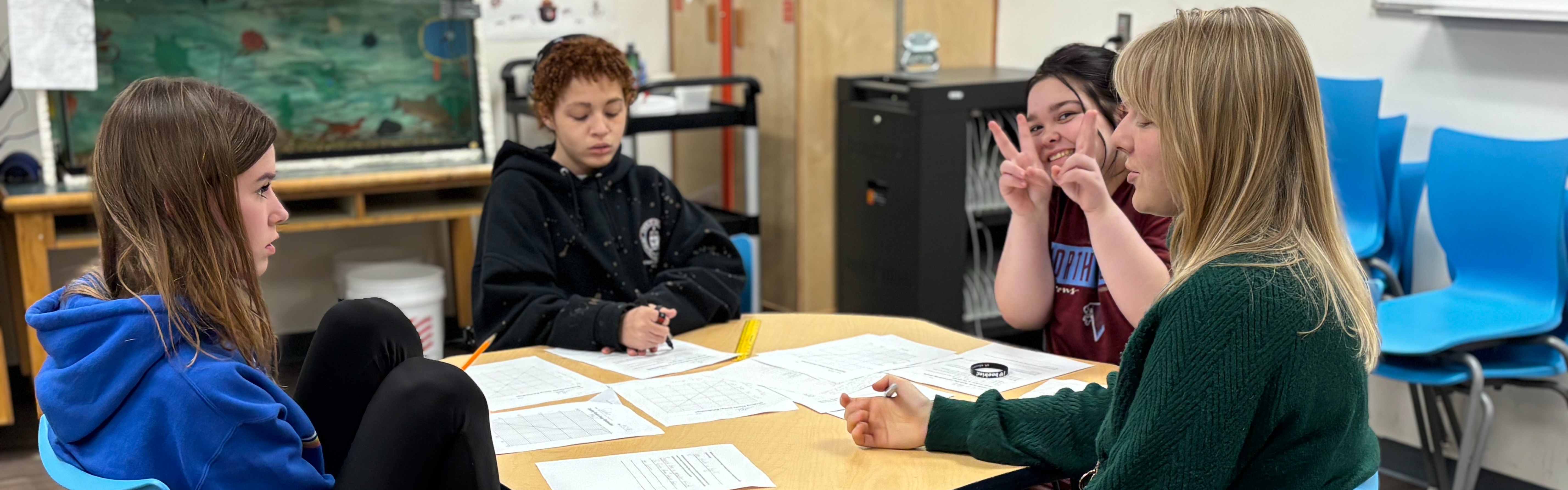 Ms. Deonigi goes over some science work with three 8th grade girls at a small table. 