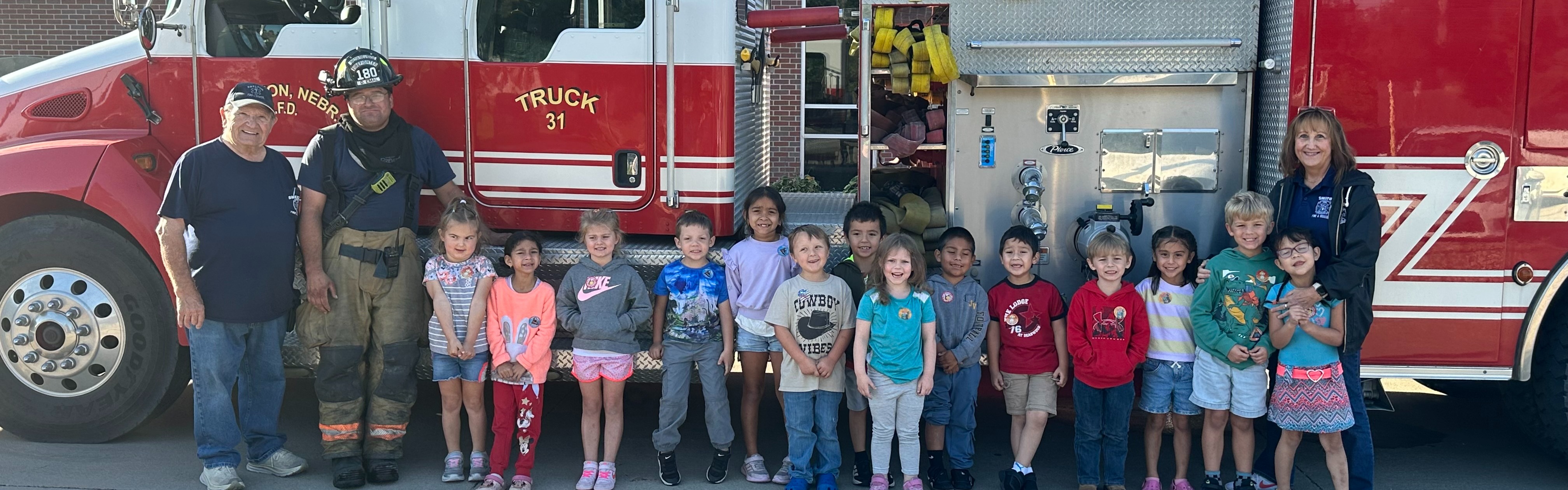 Kindergarten students standing in front of the fire trucks with the firemen
