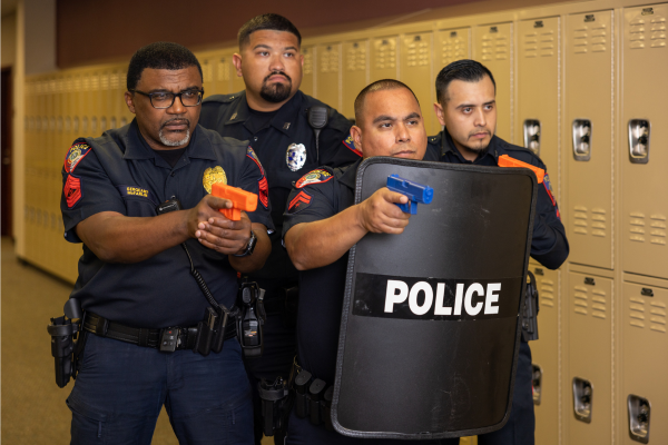 Police officers in school hallway in front of lockers holding toy guns and police shield