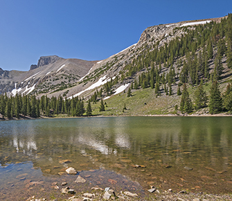 image of mountain with melting snow rising above a valley with a clear lake