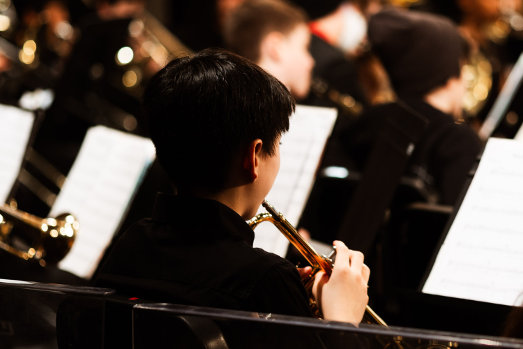 Student playing a trumpet, seated behind a music stand