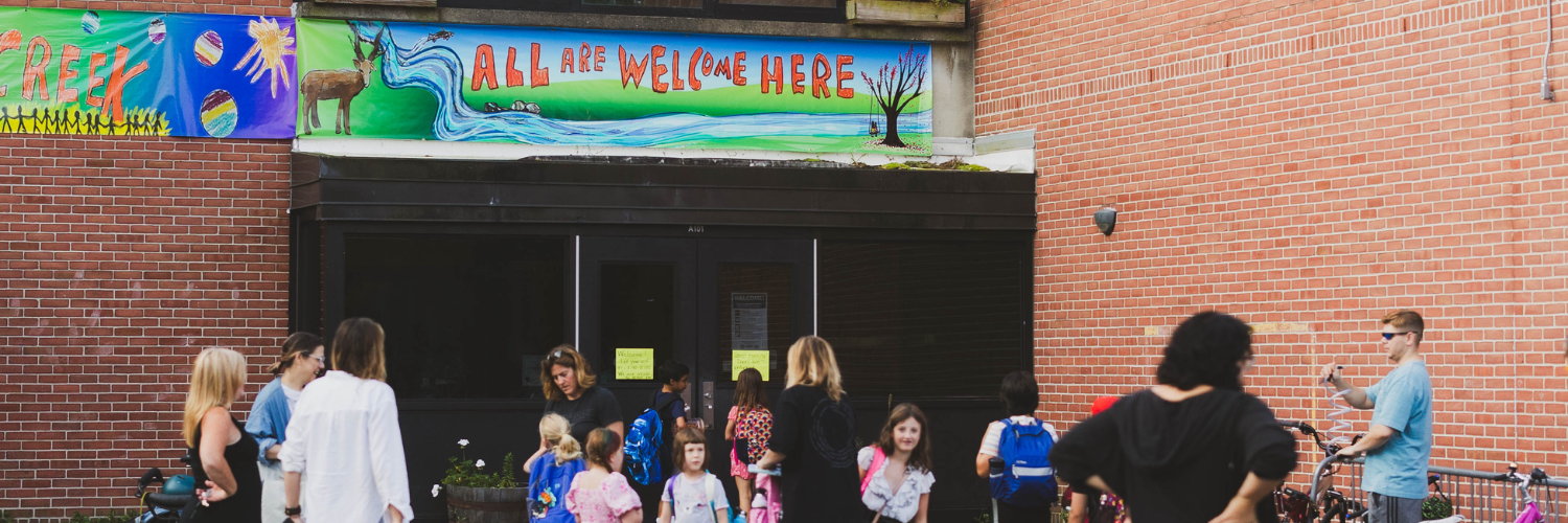 All are welcome here sign pictured on fall creek elementary while students enter the building