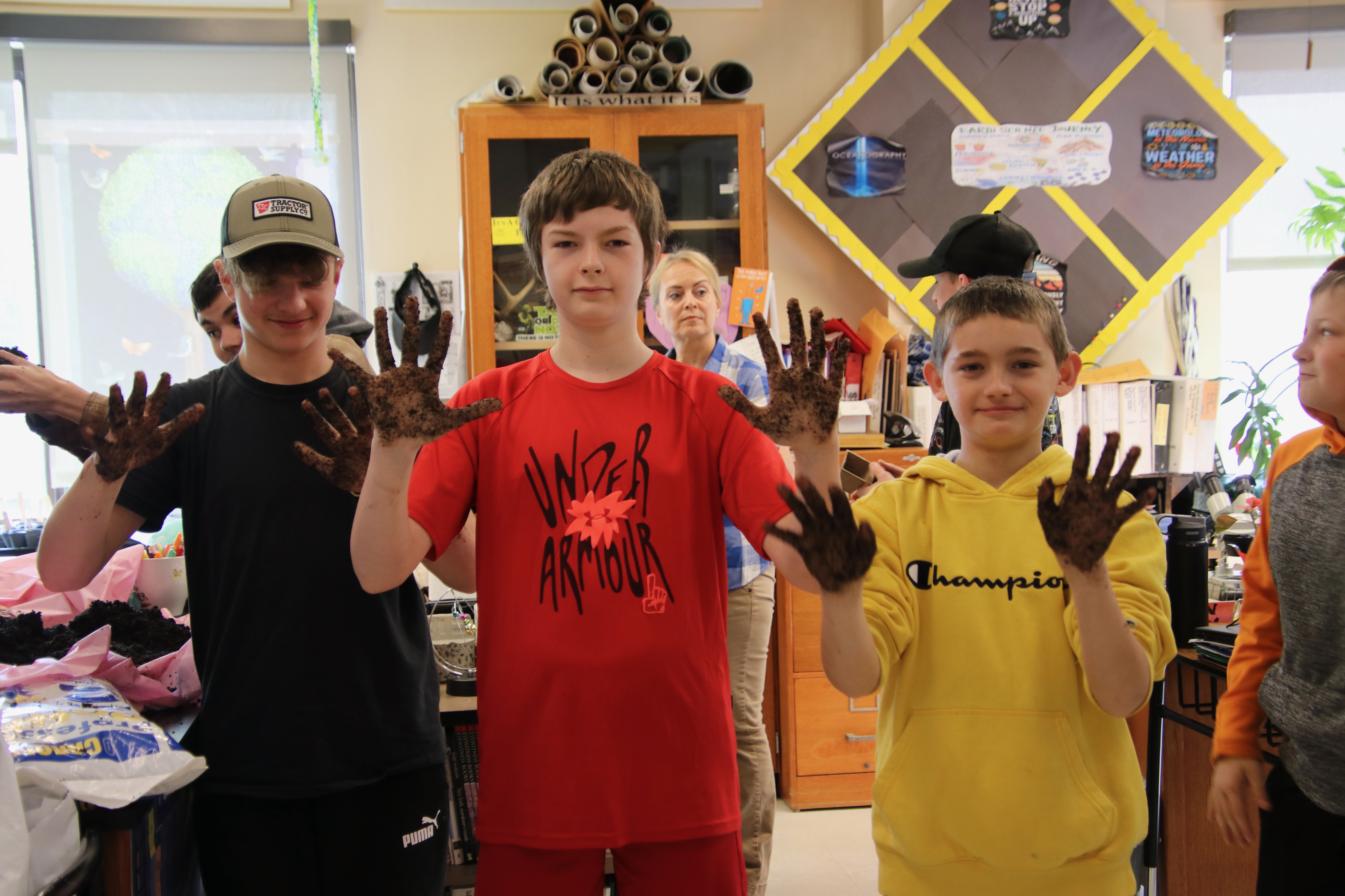 Three high school boys who have planting seedlings in a Living Environment class hold up their muddy hands