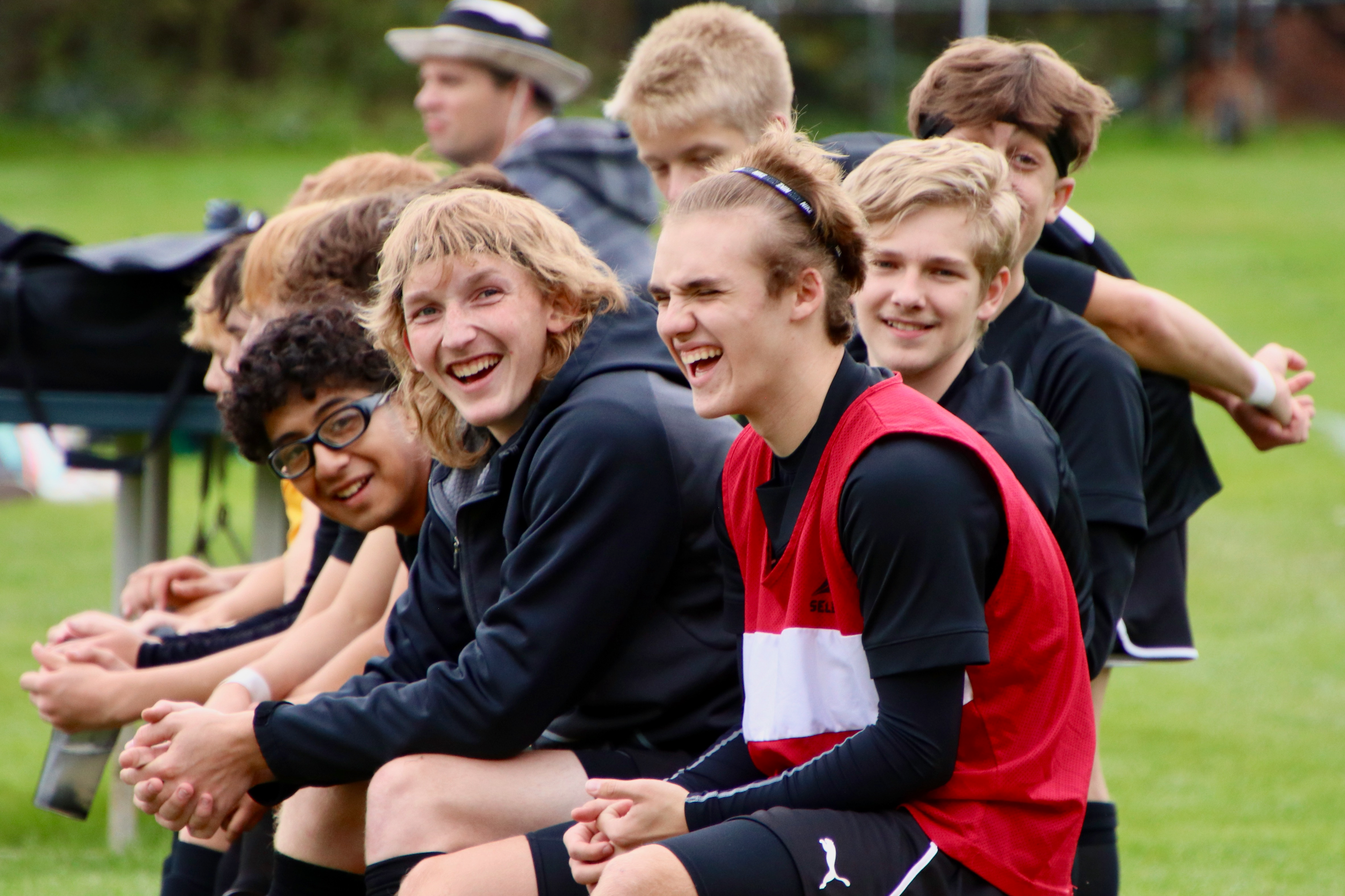 A boys soccer team sits on the bench and many laugh together