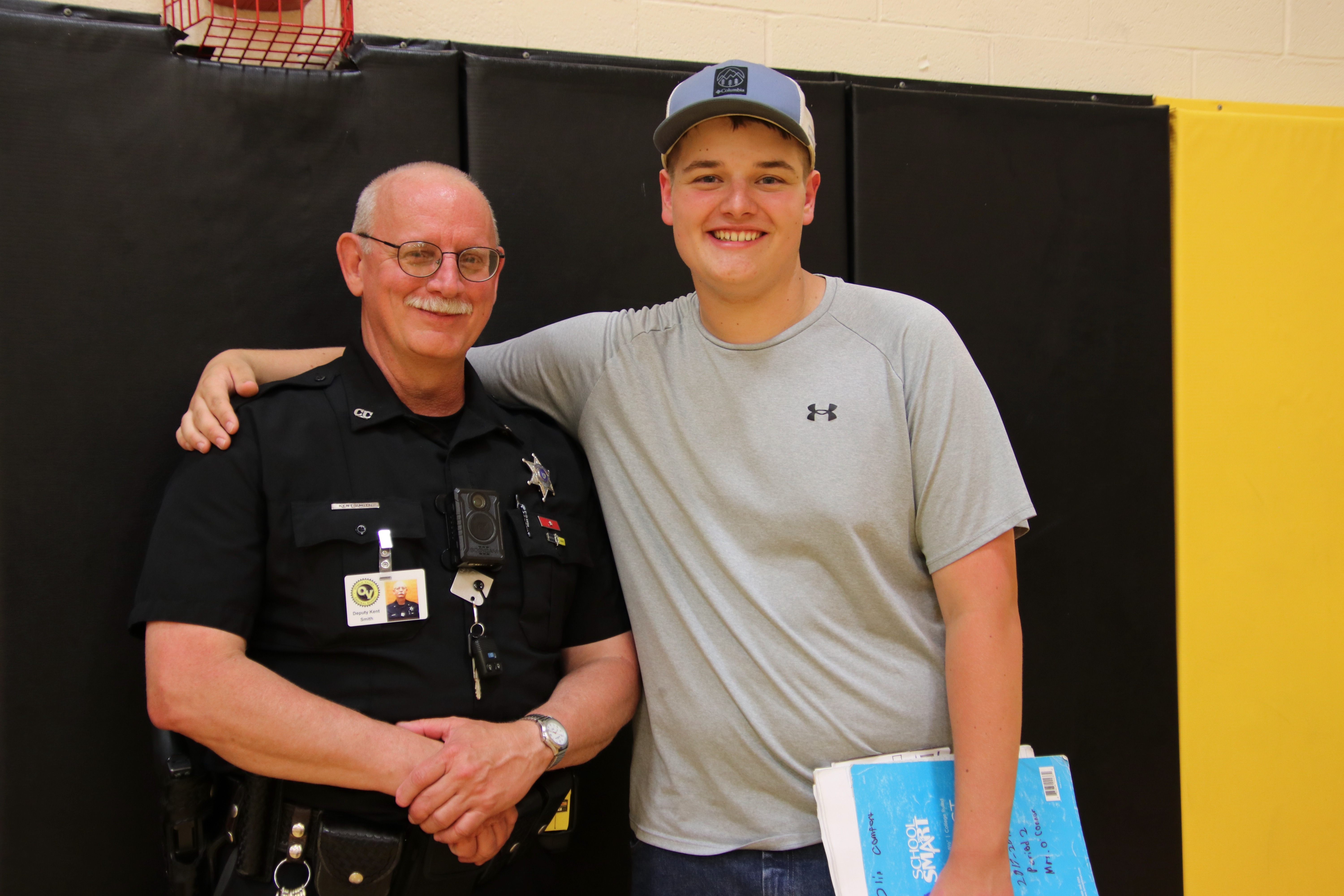 A school resource officer in his police uniform smiles with a high school student