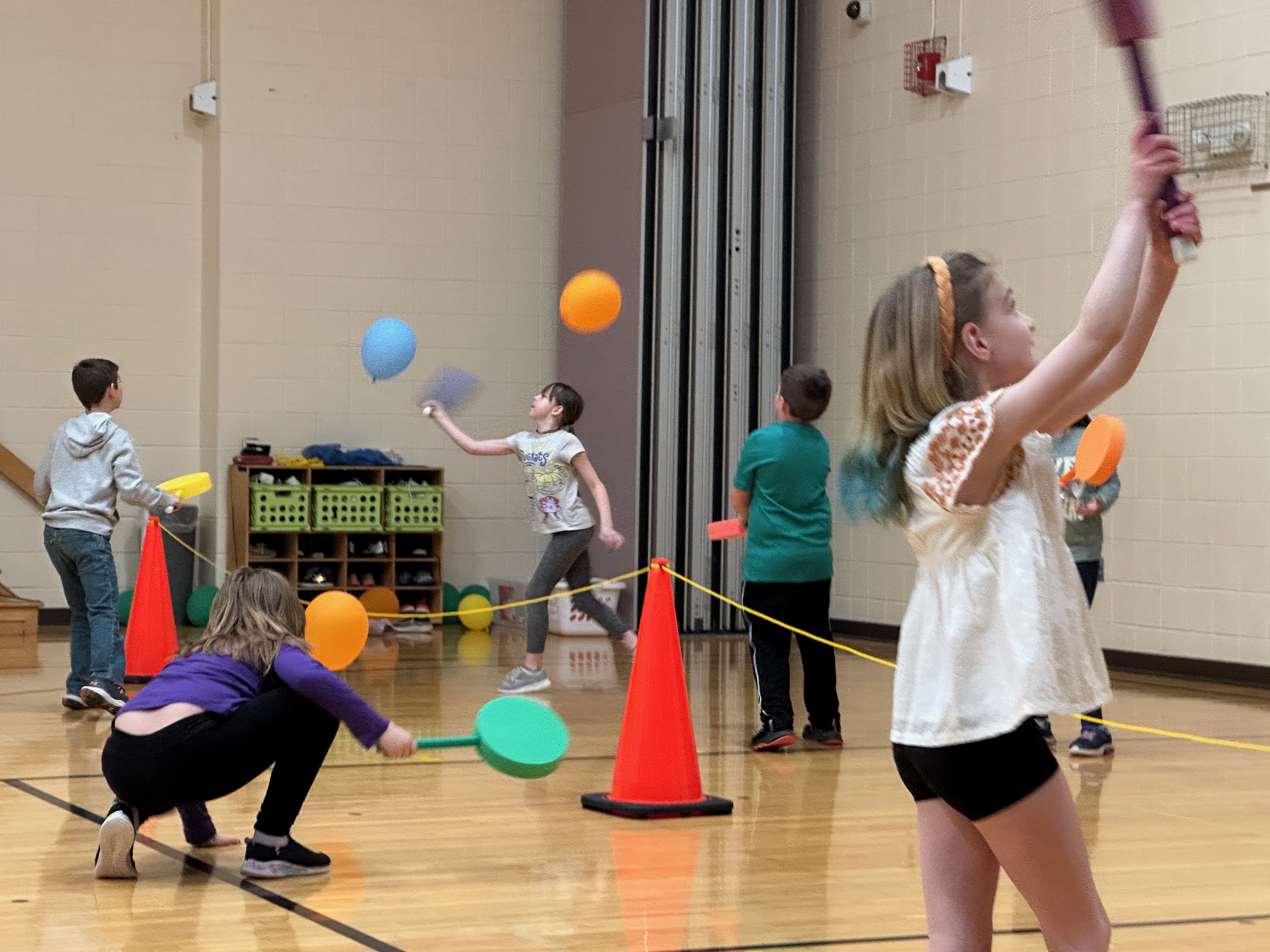 elementary students practice an activity with balloons and paddles in a phys ed  space