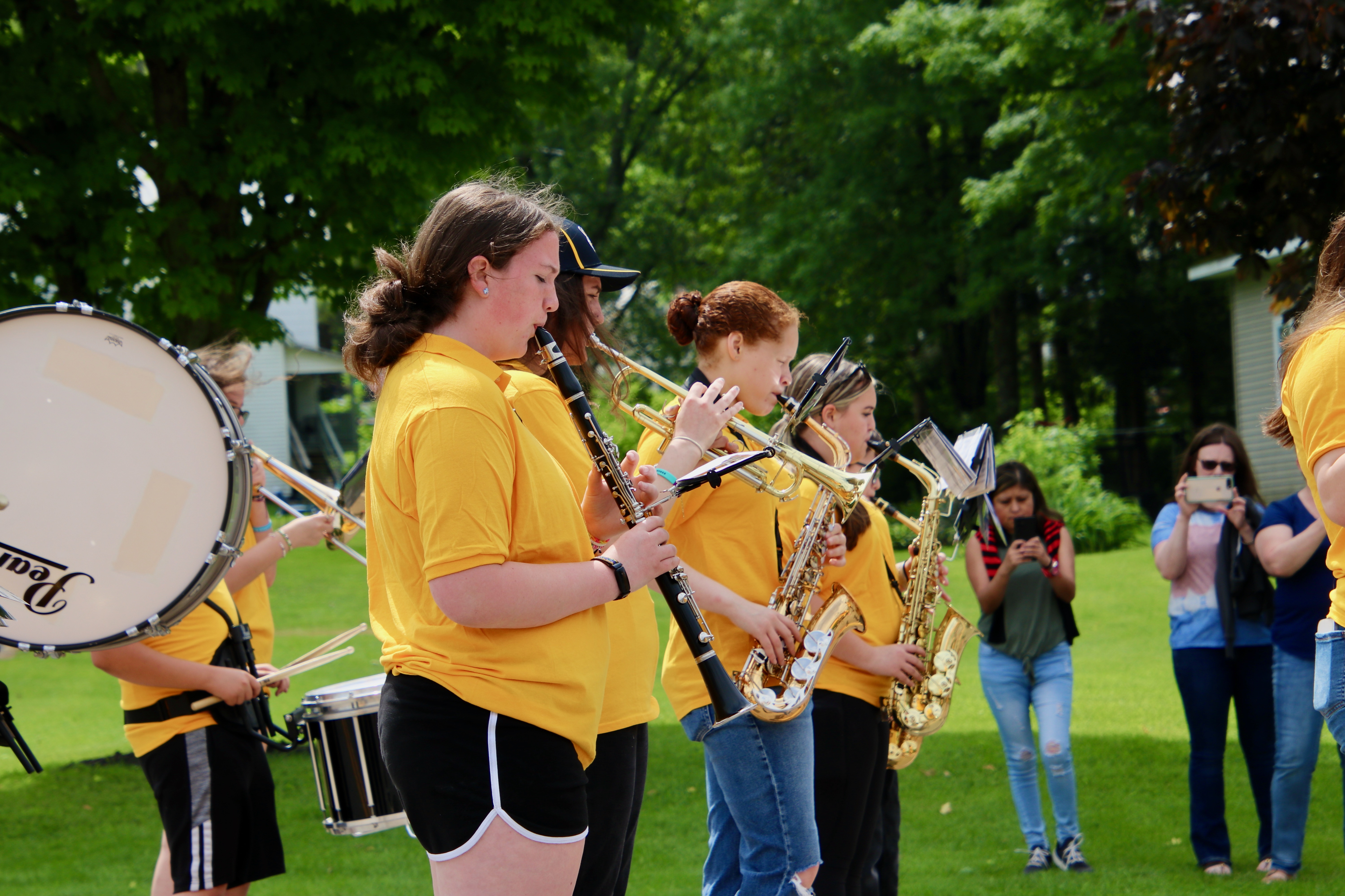 High school marching band musicians in yellow shirts perform outdoors
