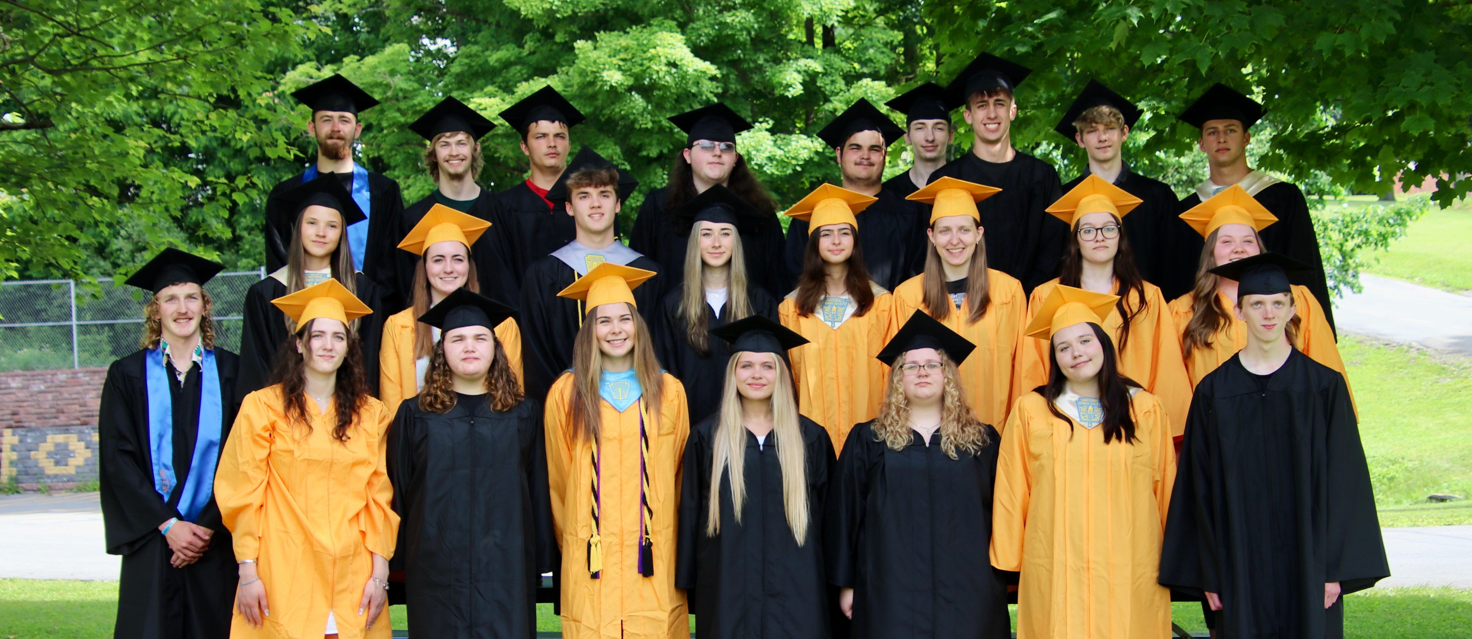 A small high school graduating class dressed in gold and black graduation gowns