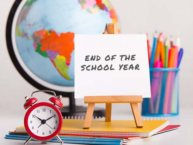 End of the School year sign on an easel, red clock, school supplies in the background