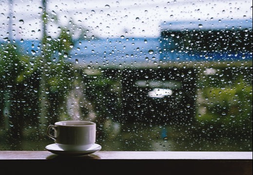 Image of a coffee cup on a window sill with rain outside