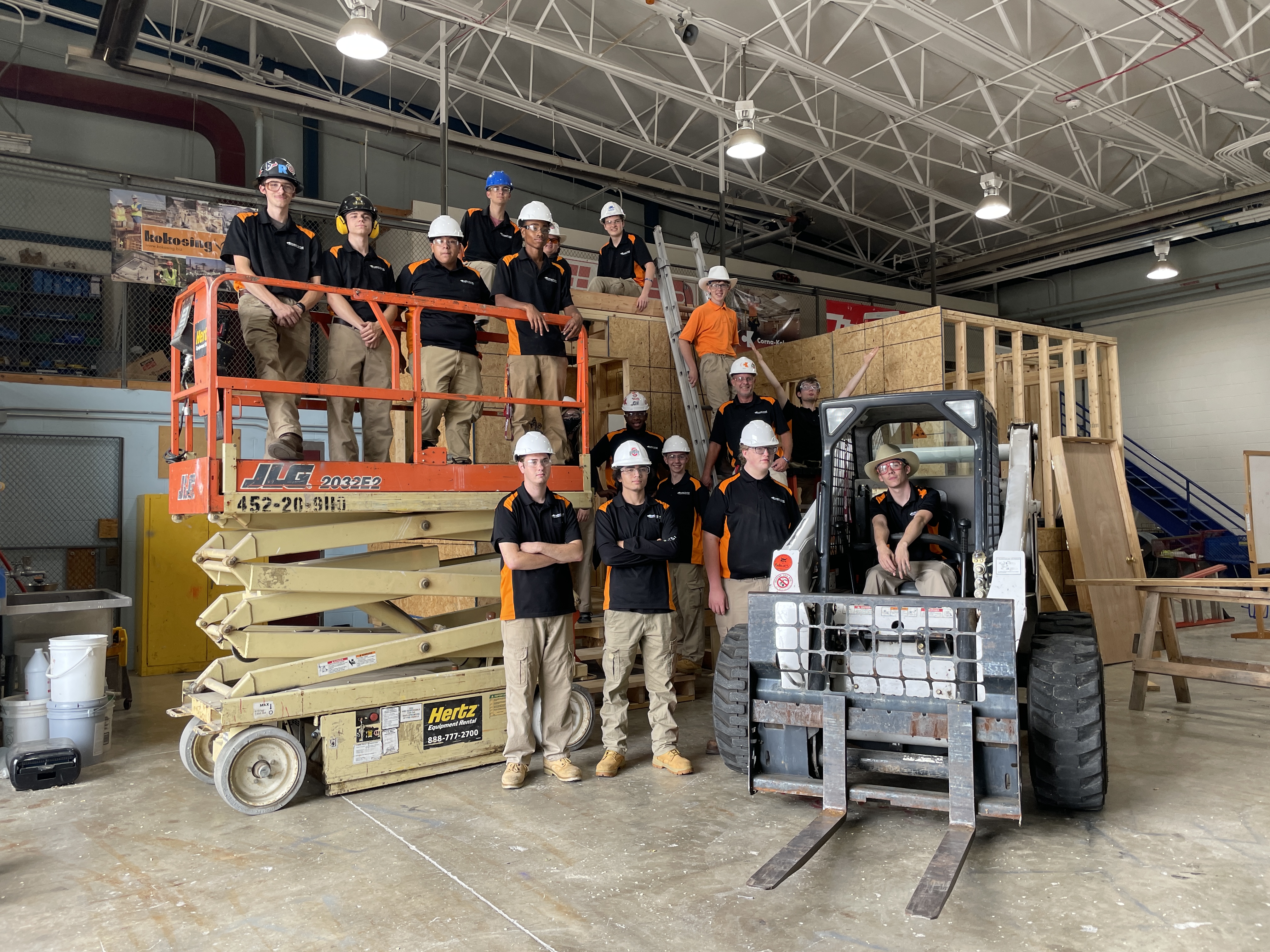 students in hardhats standing on a scissor lift and next to a fork lift