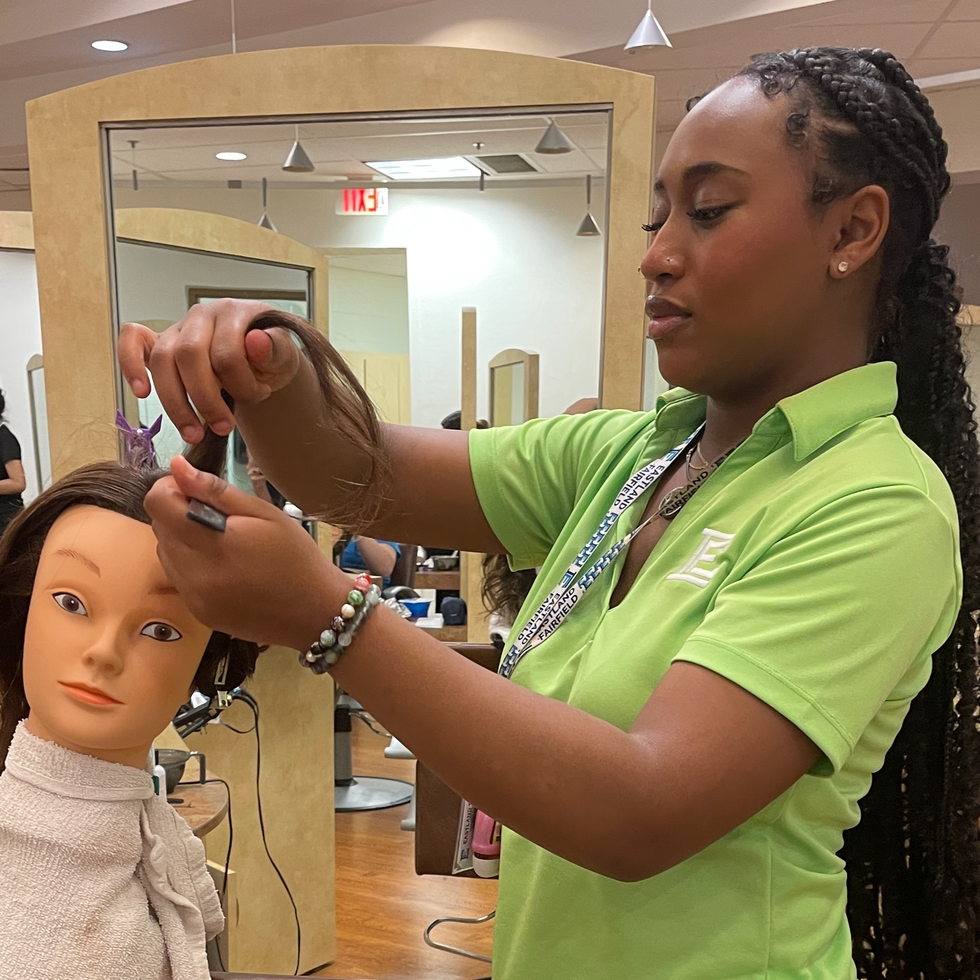 Black female student is cutting hair on a mannequin.