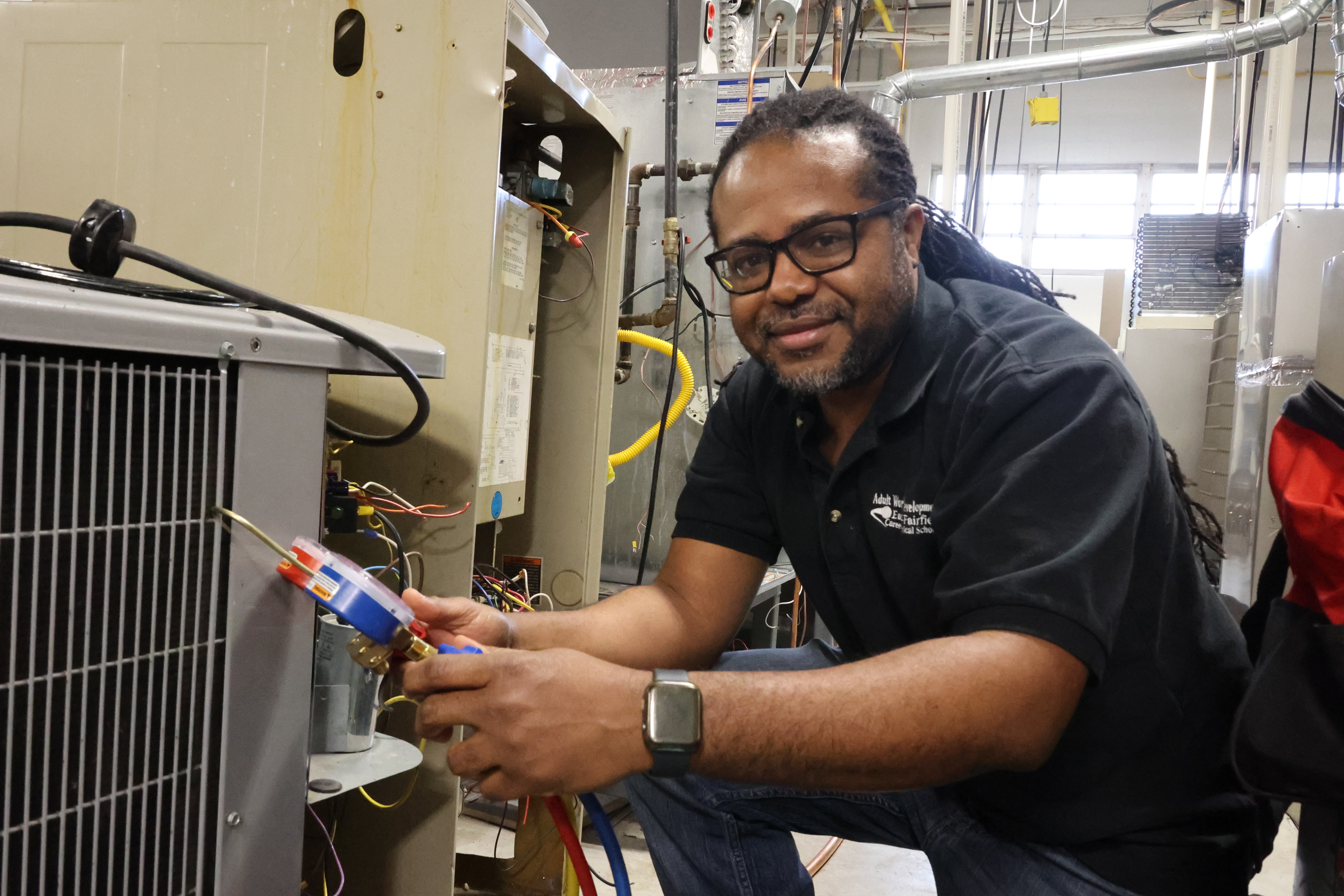 A Black male poses to the side of an air conditioning unit in his HVAC program lab.