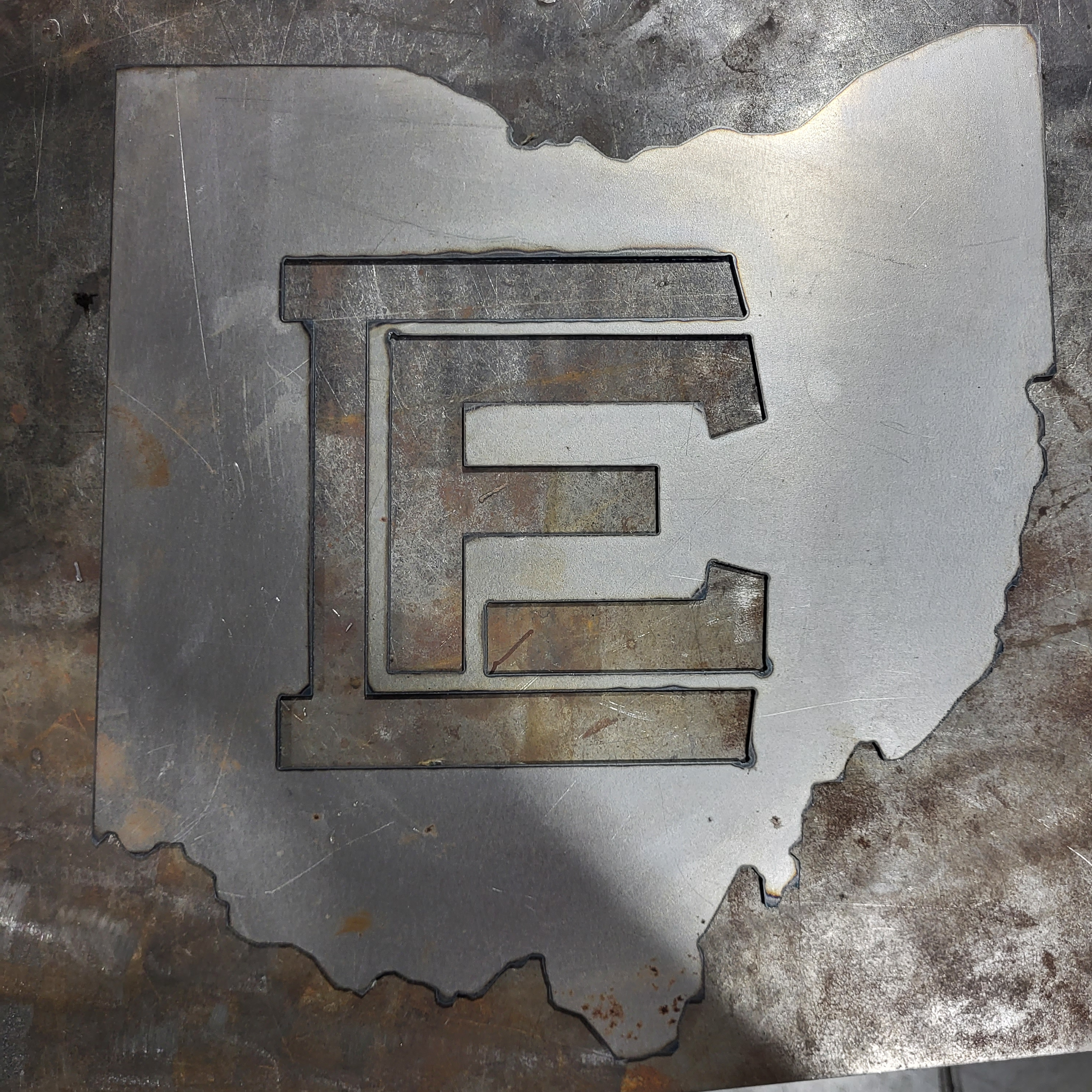 A piece of sheet metal is cut to the shape of the State of Ohio with the EFCTS logo cut out in the middle.