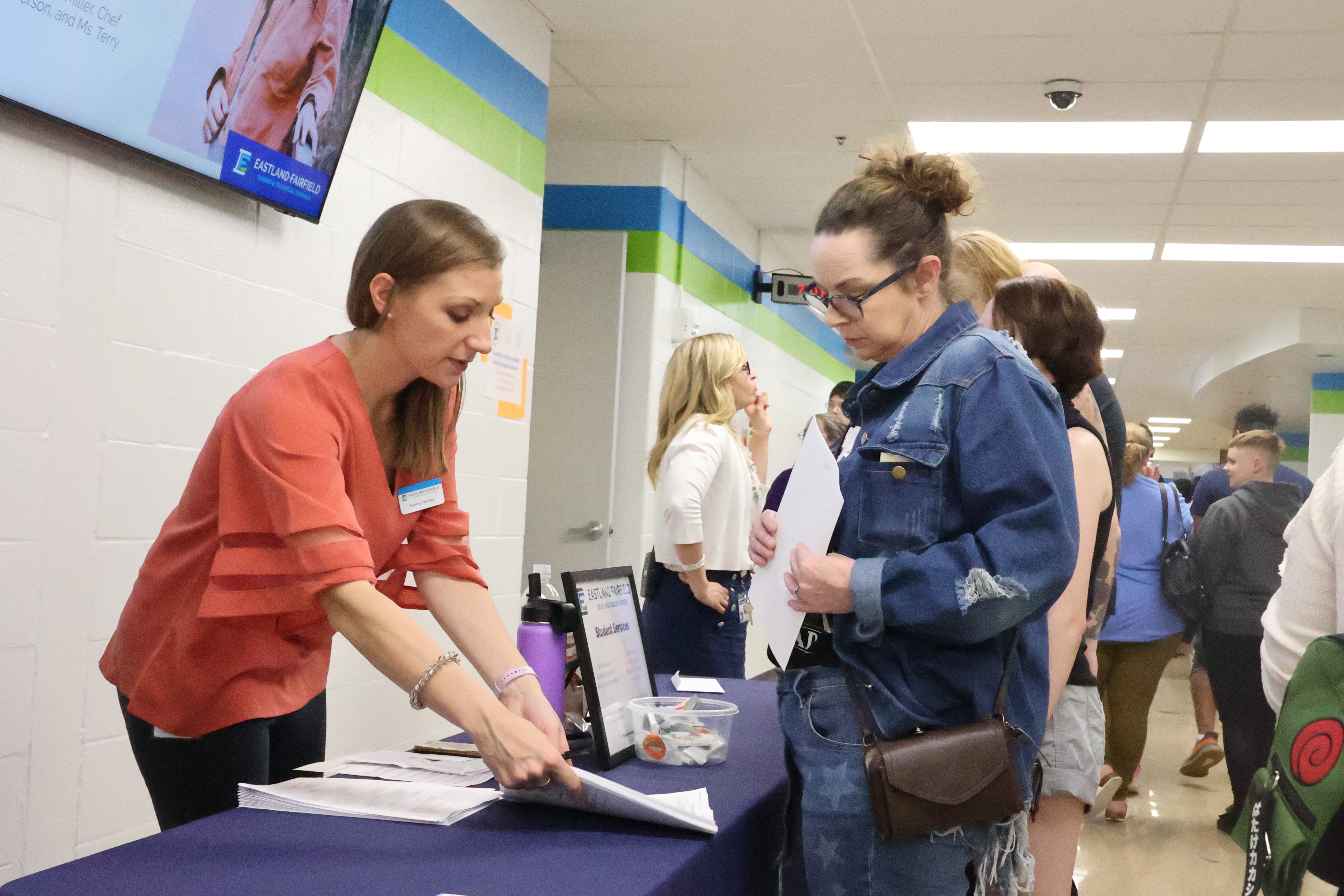 A school counselor answers questions from a prospective student's mother at a table.