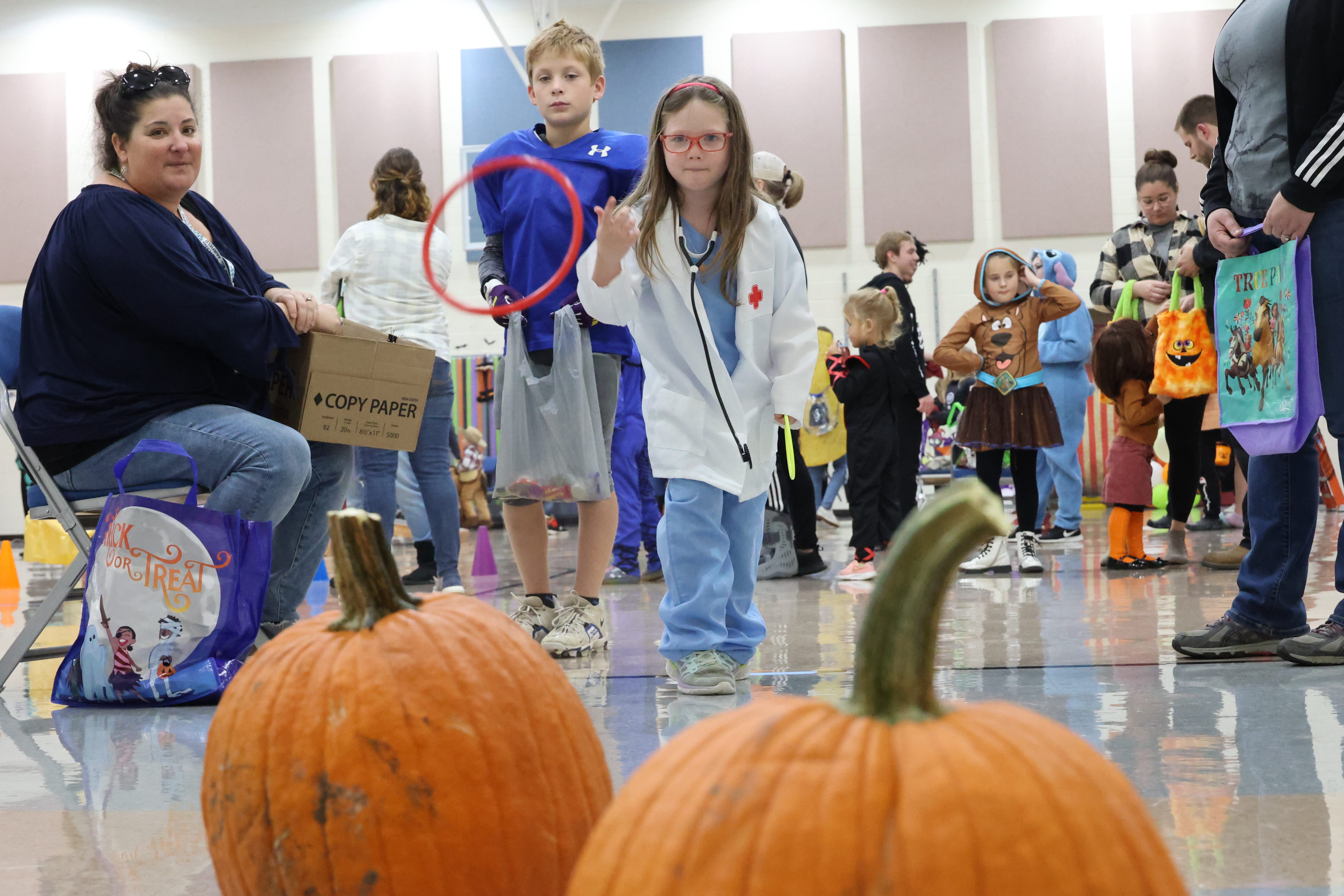 Elementary students are dressed up for Halloween and tossing rings toward pumpkin stems as part of a game.