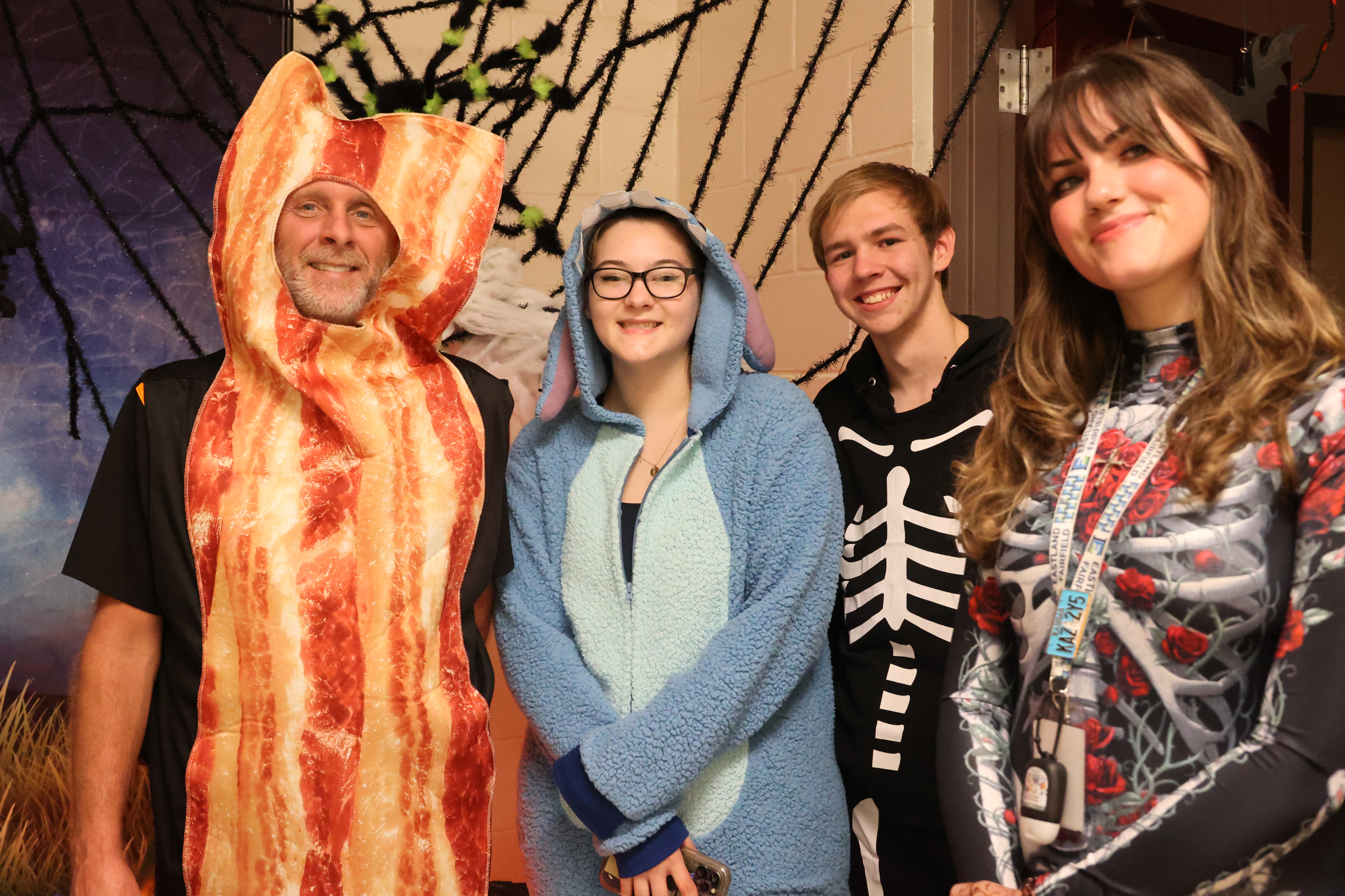 Construction instructor dressed as a piece of bacon stands with a few graduates that came back in costume.