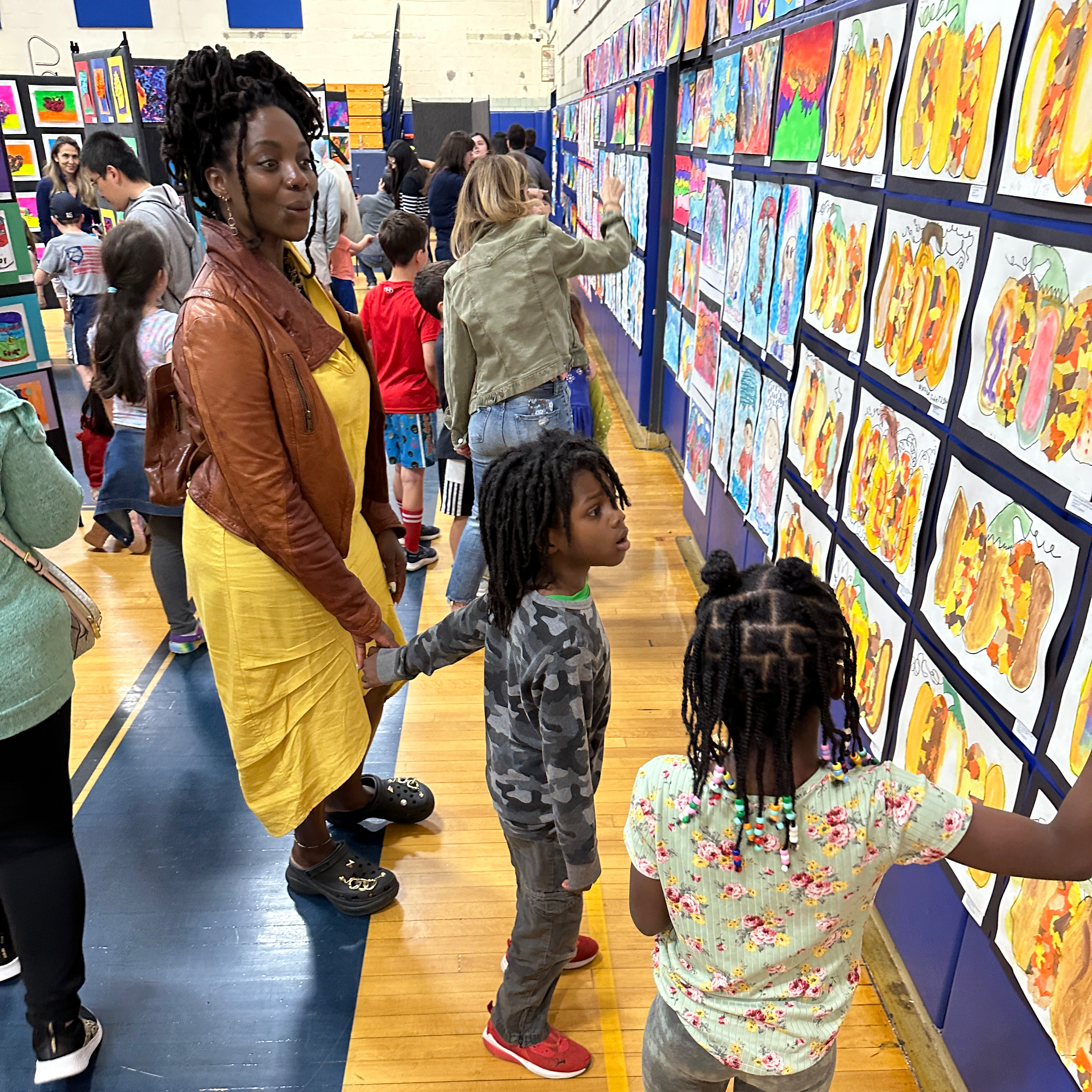 black female adult and 2 black girls looking at yellow artwork on wall