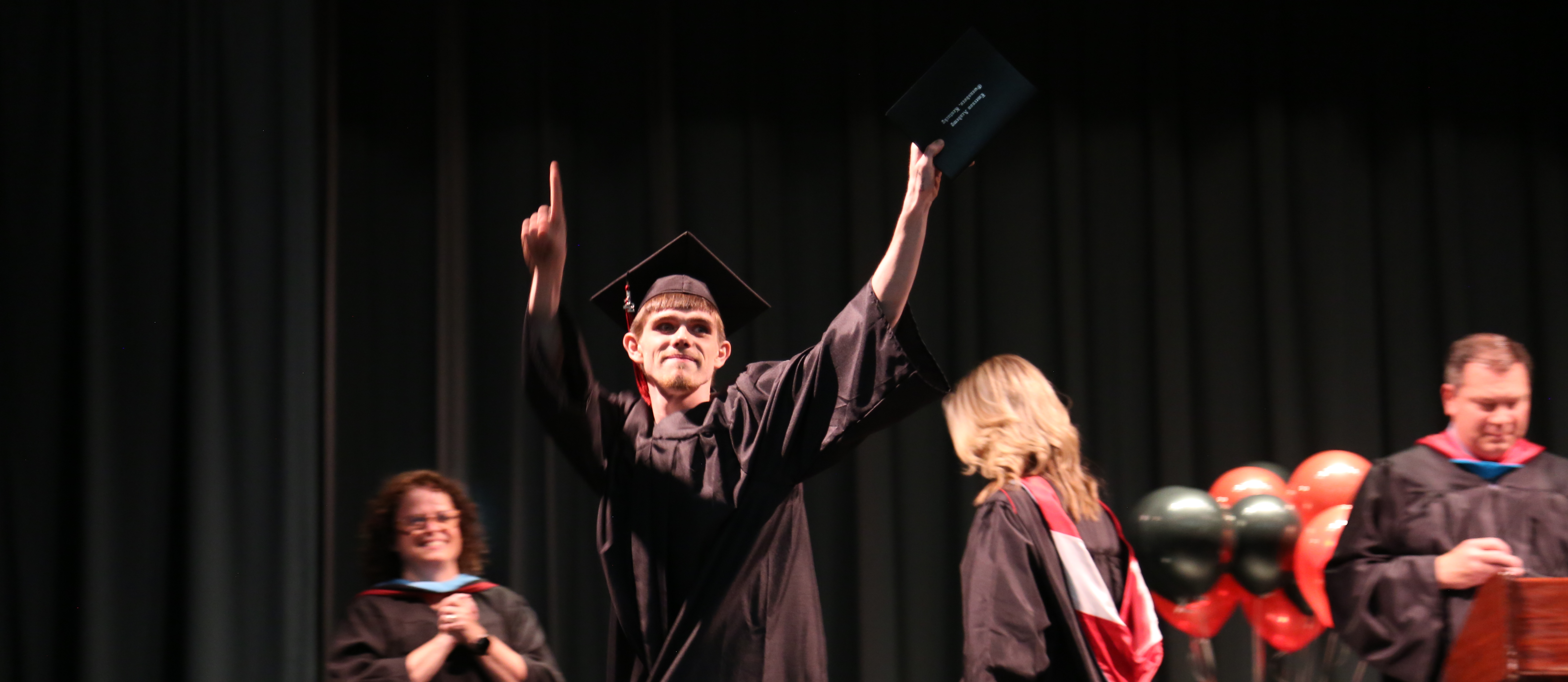 a student celebrating in cap and gown with his dipolma