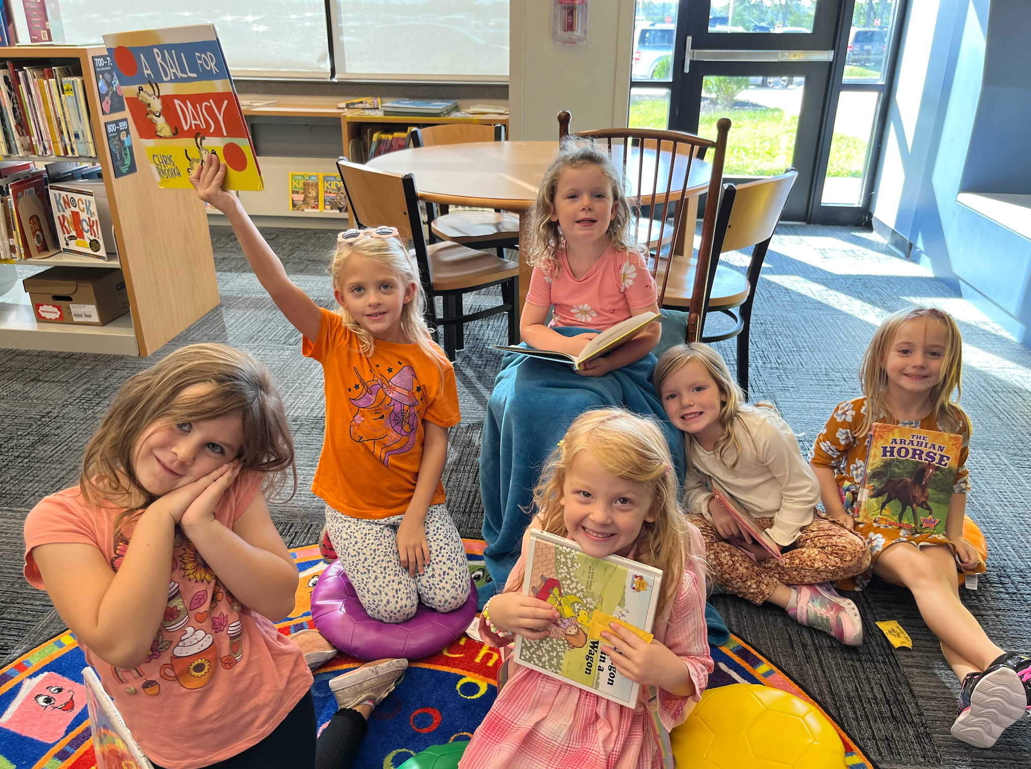 Six students seated on the floor showing books they are reading.