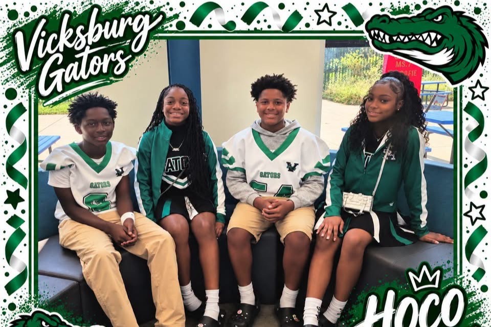 Four kids in matching green and white jerseys, sitting on a bench. "Vicksburg Gators" and "HOCO Representatives" are written above.