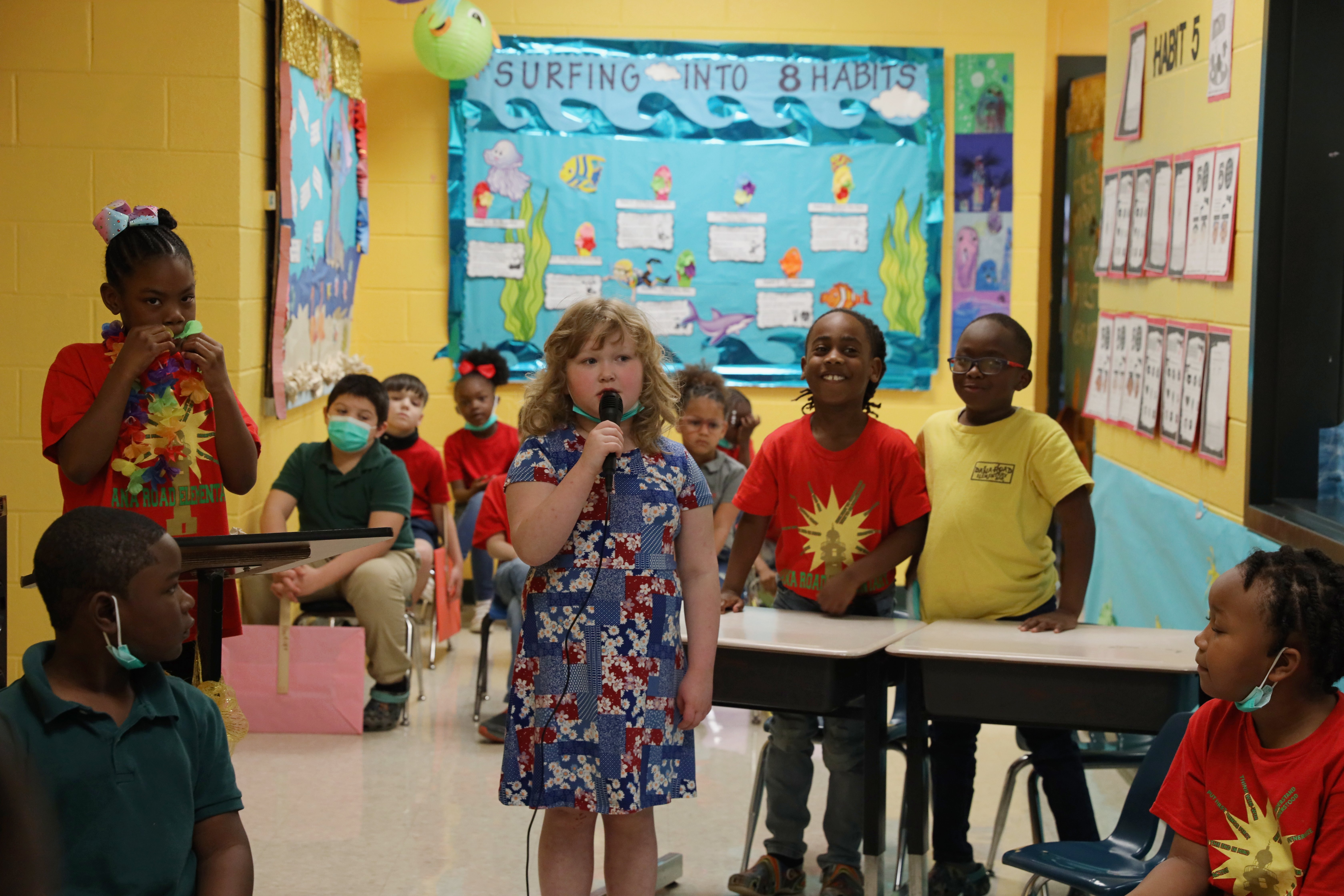 A class of Kindergarten students are performing a skit in a yellow hallway.
