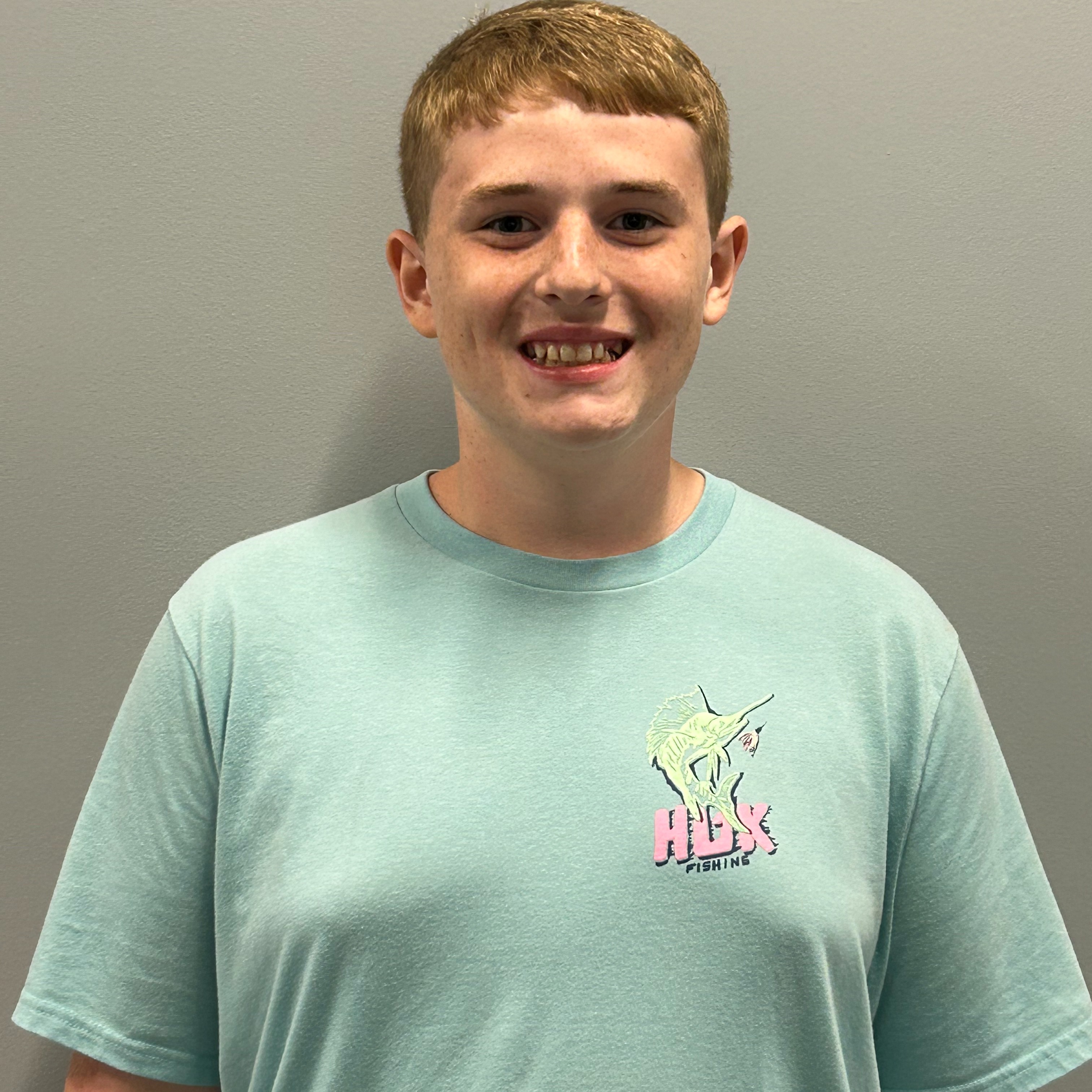 A person with short hair, wearing a light green T-shirt with a unicorn and the word "HEX" on it, is smiling.