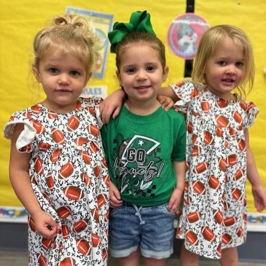 two girls wearing dresses with footballs on them and a girl in a green shirt standing in the middle