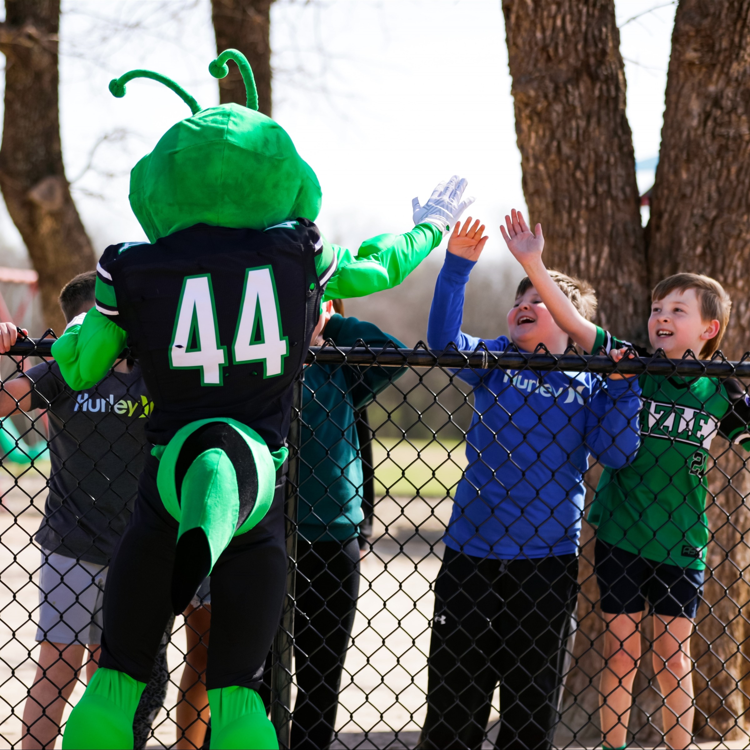 Buzzy standing at fence high-fiving elementary boys