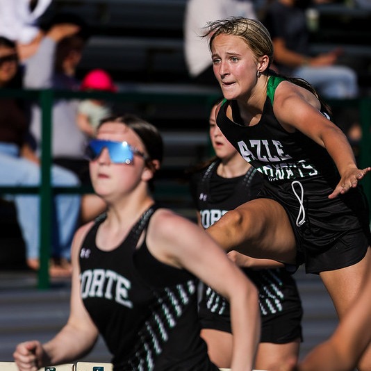 girls in track uniforms running hurdles