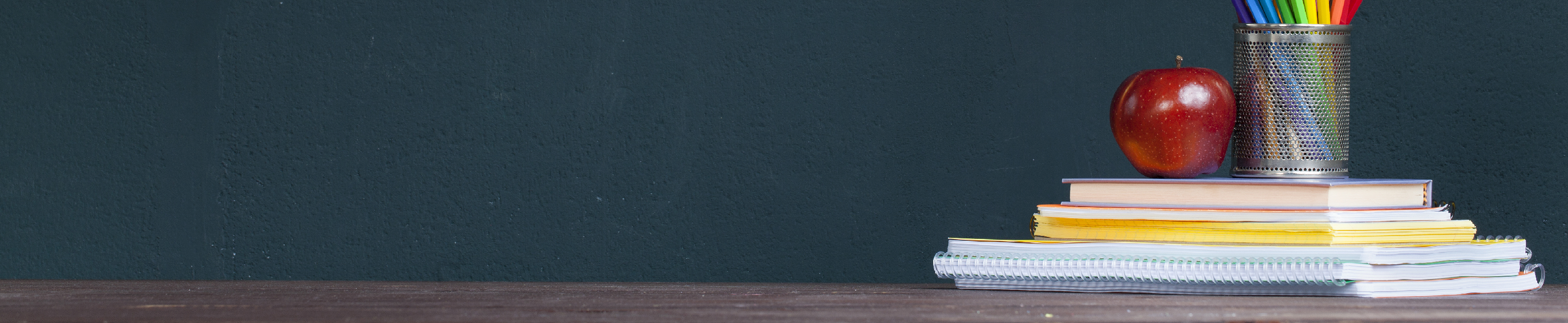 An image of an apple, pens and a stack of books in front of a blackboard.