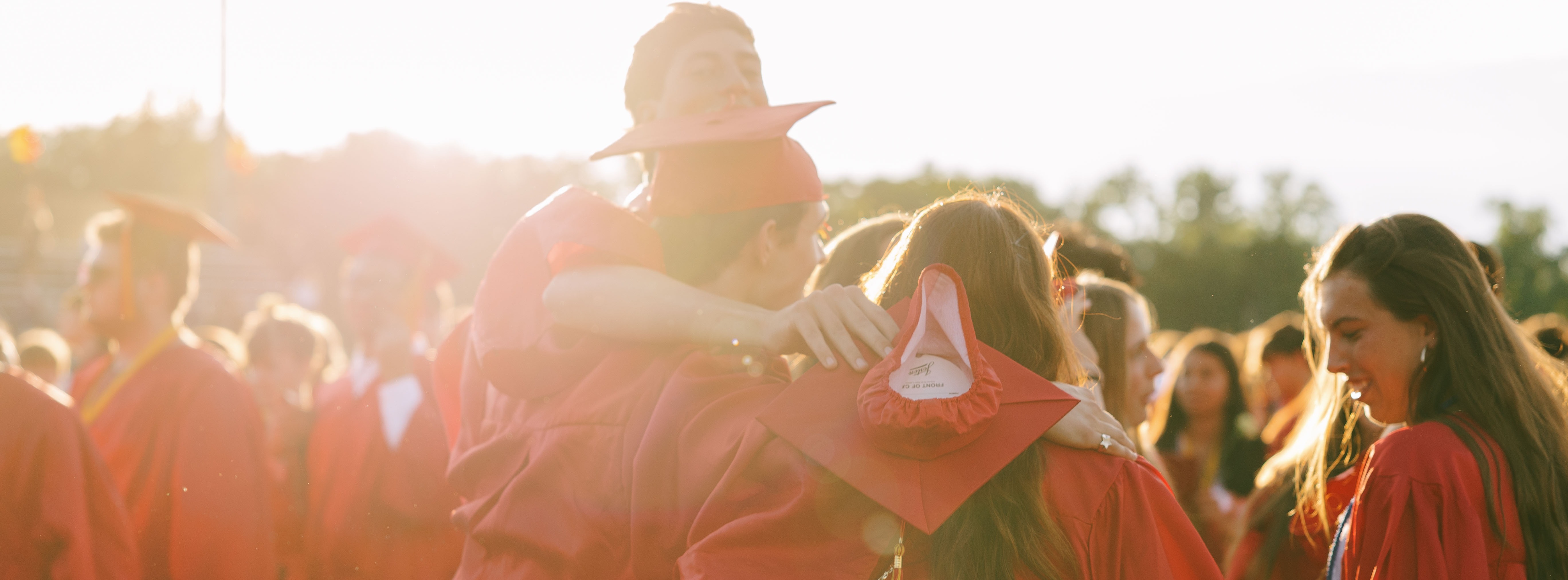 A group of individuals in red graduation robes and hats gathered together in an outdoor area.