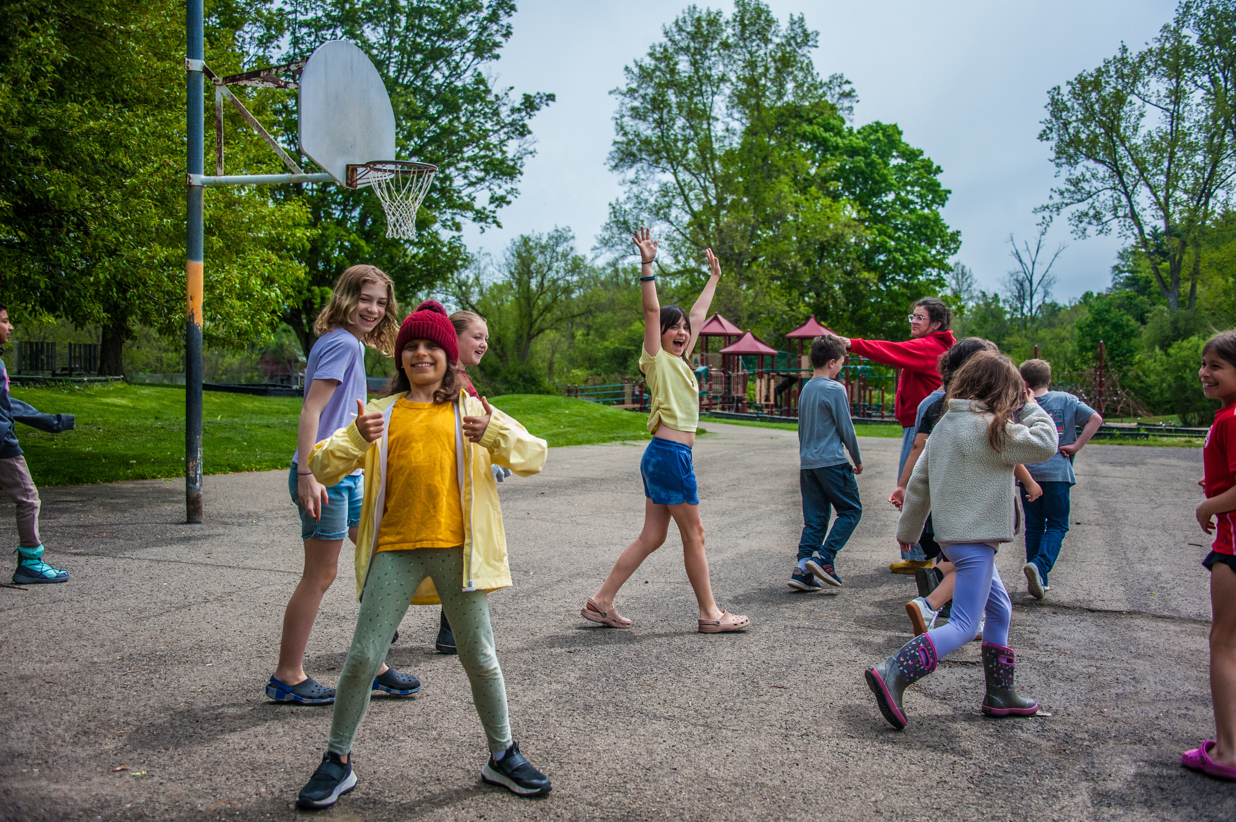 Group of children wearing sneakers and colorful clothes dancing outside near a basketball court.