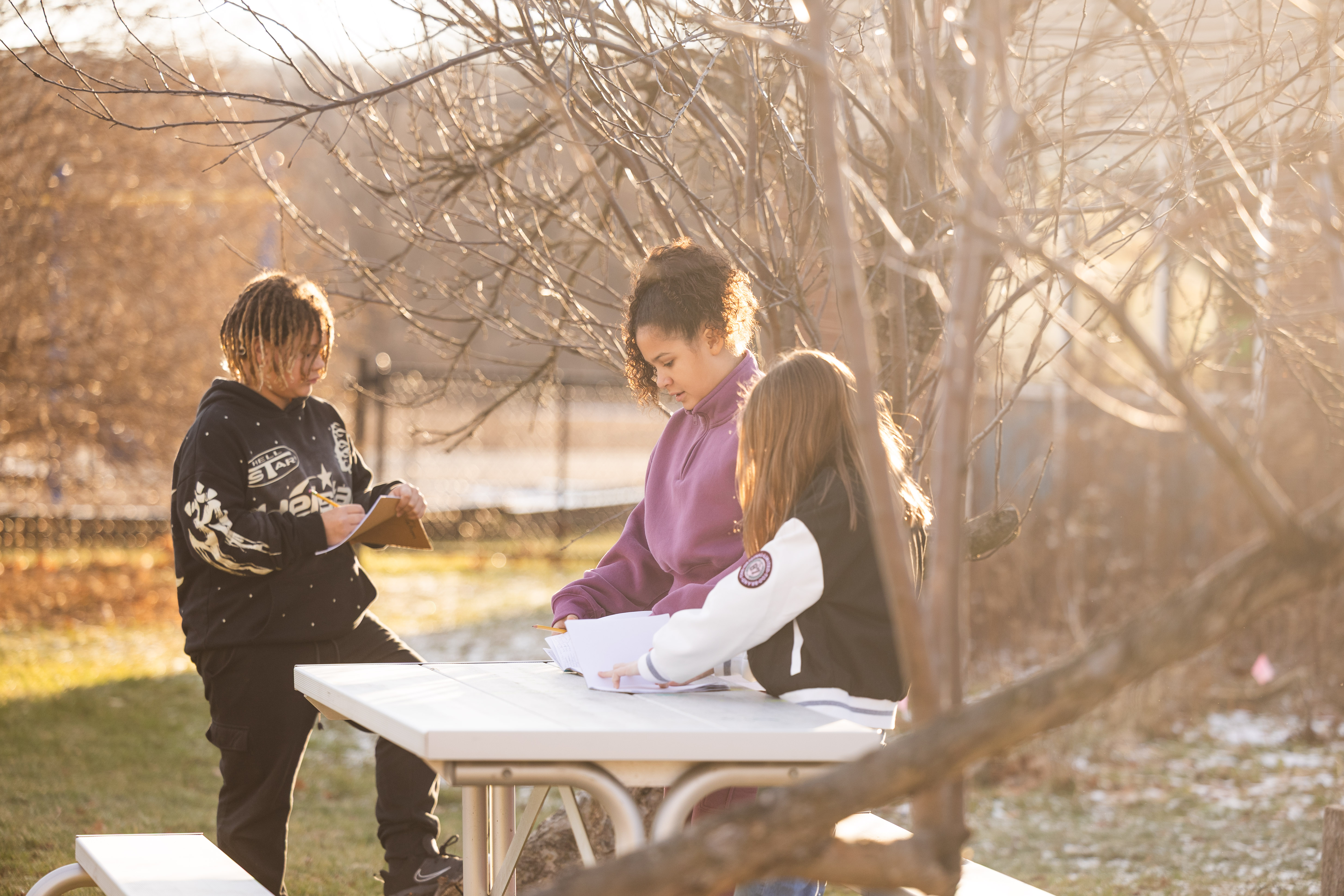 Three 5th graders work on a weather project at an outdoor table