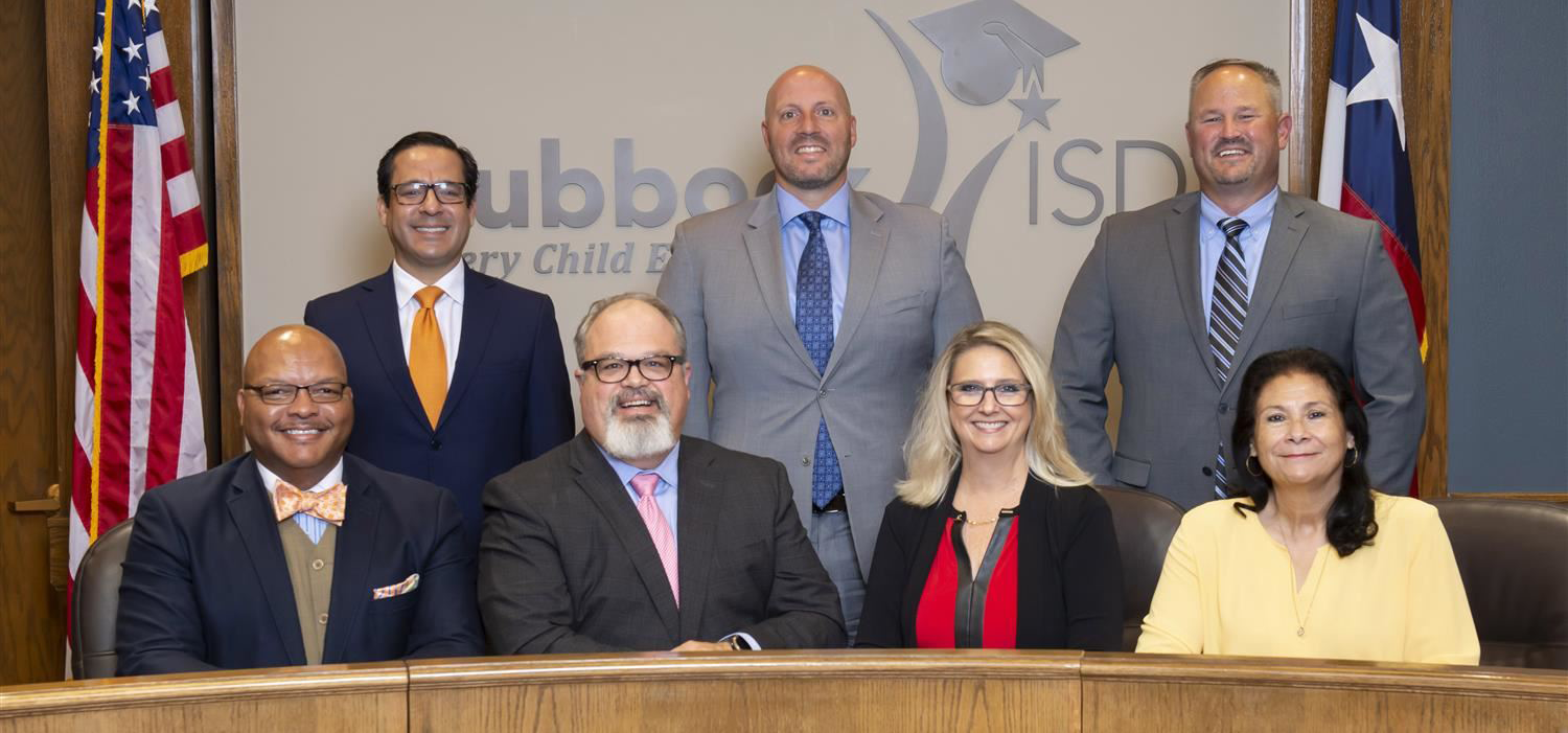 seven board members standing in front of Lubbock ISD logo in the board room