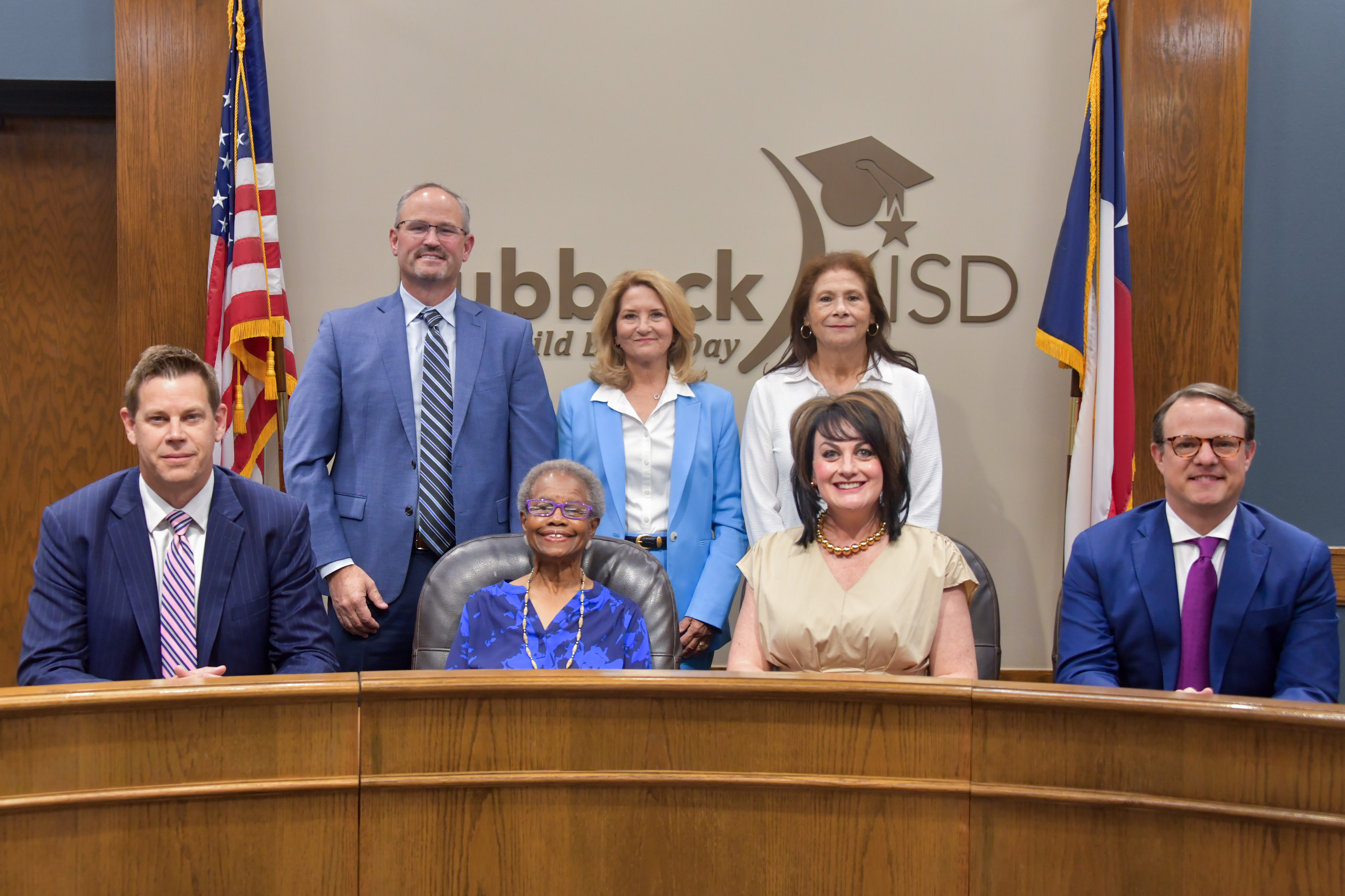 seven board members standing in front of Lubbock ISD logo in the board room