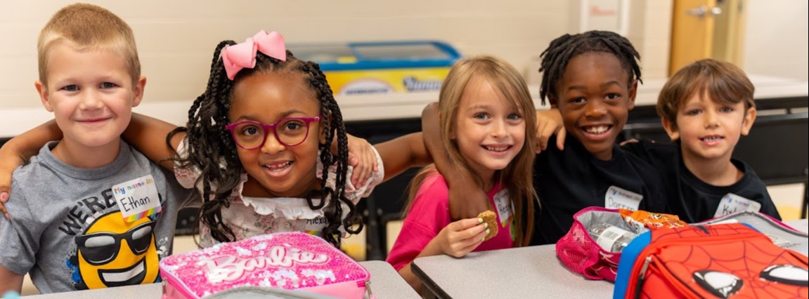 Five students at lunchroom table smiling