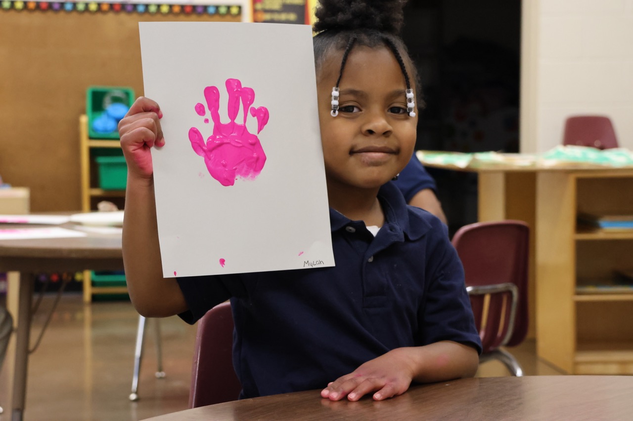 Pre-K student holding up pink painted handprint