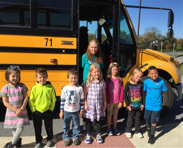 7 young students standing in front of school bus with bus driver