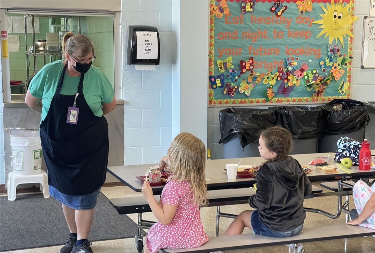 Cafeteria worker monitoring students eating lunch at the table