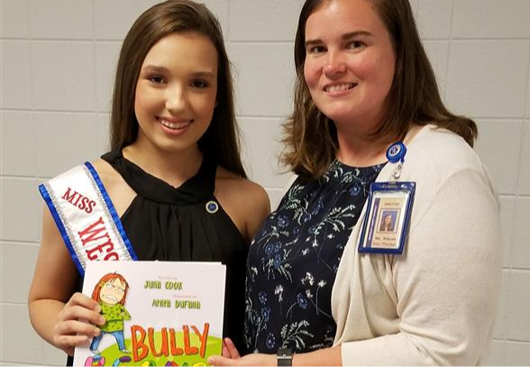 Teacher taking a picture with a student holding a book that says bully