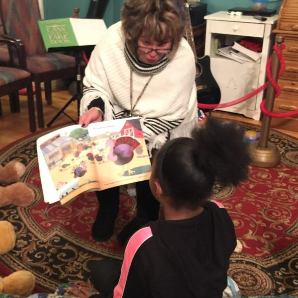 Woman reads a read aloud to class and lets girl look at the pictures in the book