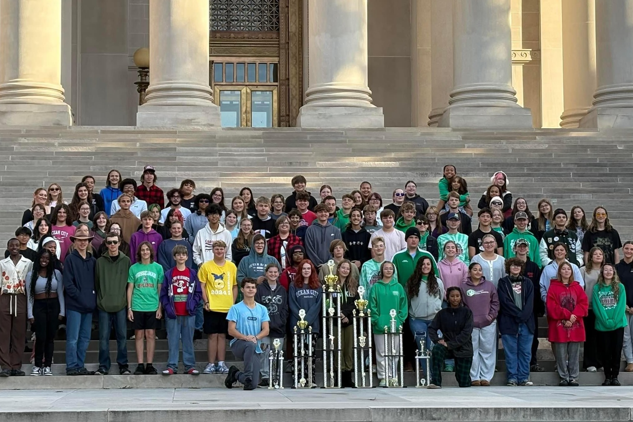 students with trophies in front of building