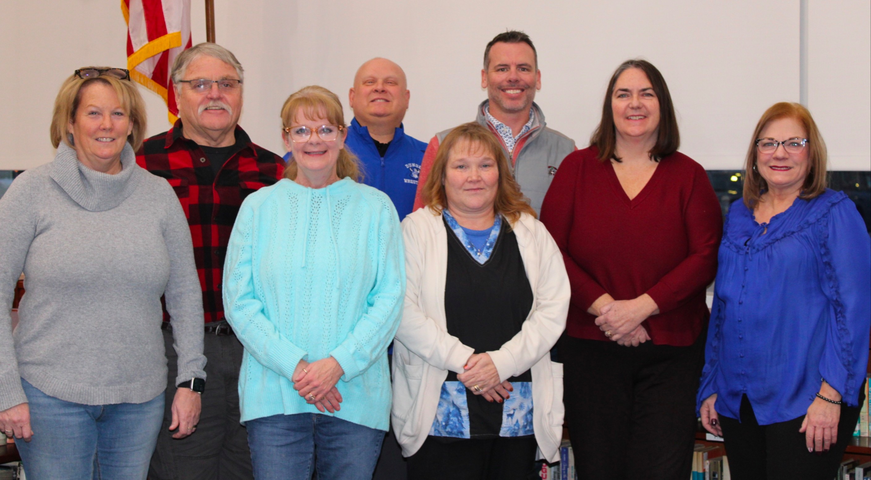 board of education posing underneath American Flag Left To Right: Front Row: Crystal Root, Trustee; Kimberly Wilkins, Trustee. Back Row: Patricia Motylinski,trustee; Tara Mckenzie, Treasurer; Christian Freshour, President; Jacey Carner, Secretary; Scott Leach, Superintendent; Keith Pilbeam, Vice-president. 