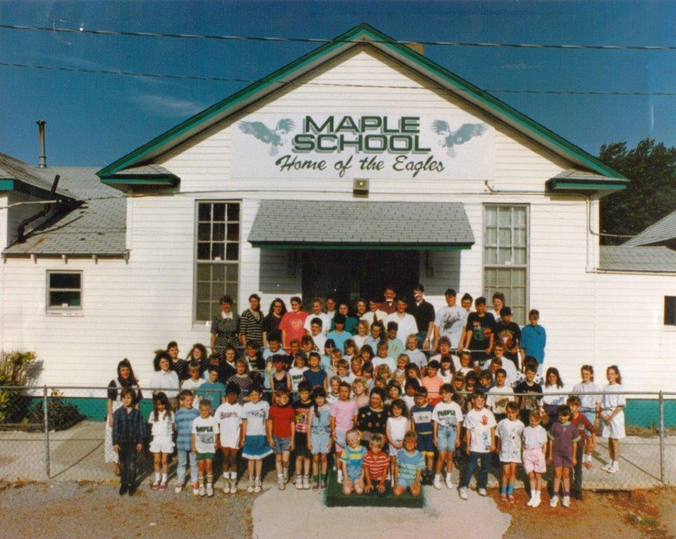 Children standing outside of a schoolhouse that says "Maple School: Home of the Eagles"