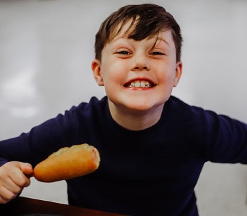 a boy smiling and holding a corndog