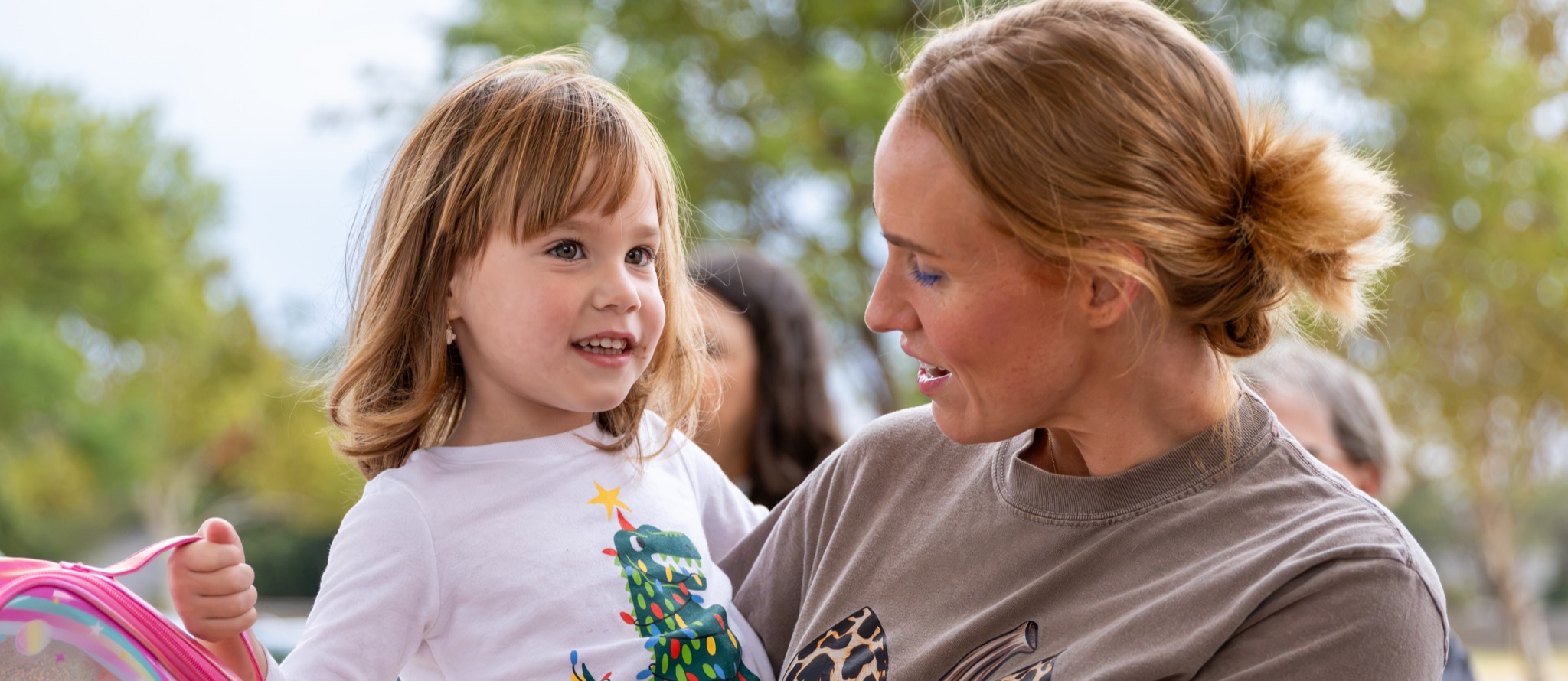 A parent holds her smiling child as she drops her off for school
